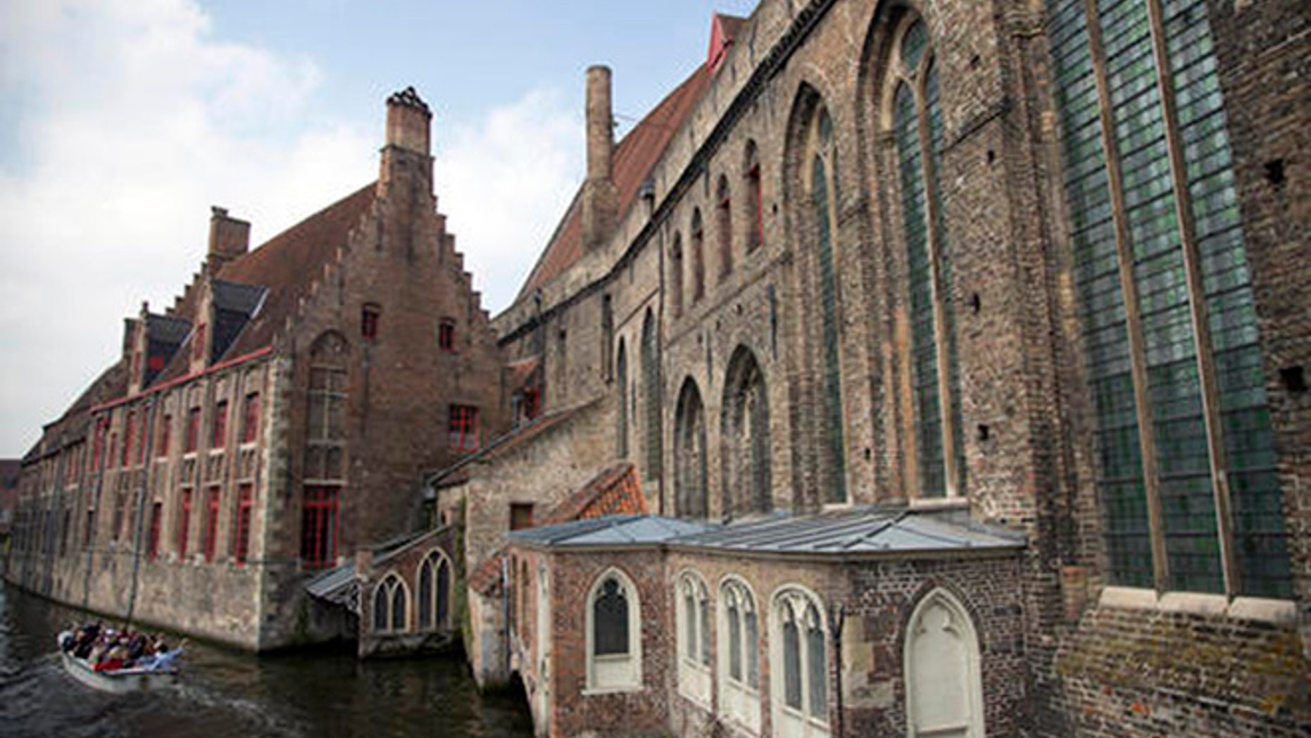 Tourists ride in a boat down a main canal past the Hospital St. Jan in Bruges, Belgium on Thursday, May 26, 2016.