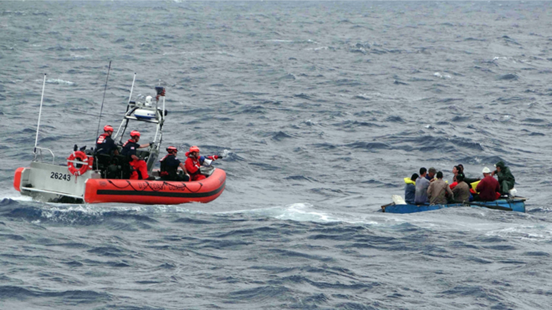 Coast Guard personnel left, try to assist a group of Cuban migrants on a makeshift vessel in the Florida Straits.