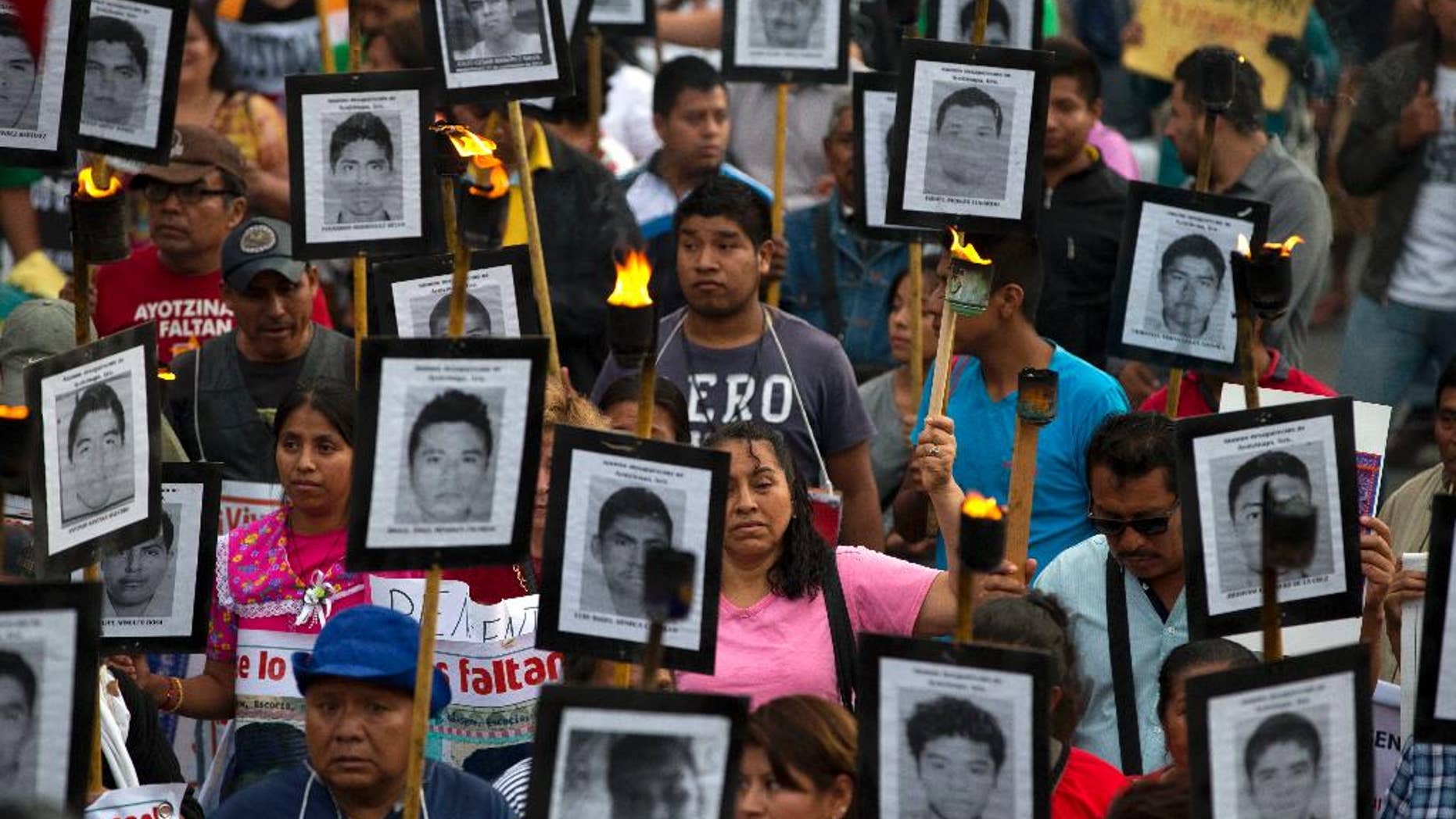 FILE - In this April 26, 2016 file photo, family members and supporters of 43 missing teachers college students carry pictures of the students as they march to demand the case not be closed and that experts' recommendations about new leads be followed, in Mexico City. The most recent forensic investigation of the southern Mexico garbage dump where the government says 43 students were incinerated did not confirm there was a fire there that night. It shows the experts found evidence the Cocula dump had been the site of at least five fires, but could not determine when. Remains of 17 people were also found, but it was unknown when they were burned. (AP Photo/Rebecca Blackwell, File)