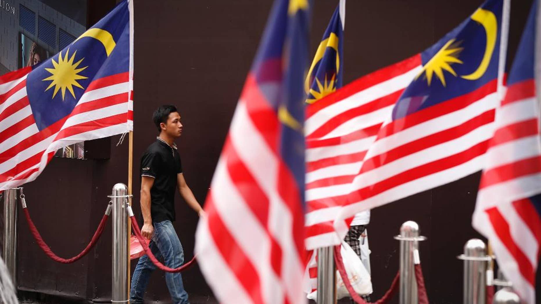 A man walks by displays of Malaysian national flags outside a shopping mall in Kuala Lumpur, Malaysia Wednesday, Aug. 12, 2015. A Malaysian opposition party Wednesday filed a civil lawsuit against Prime Minister Najib Razak for alleged election offenses involving $700 million in his bank accounts. (AP Photo/Vincent Thian)