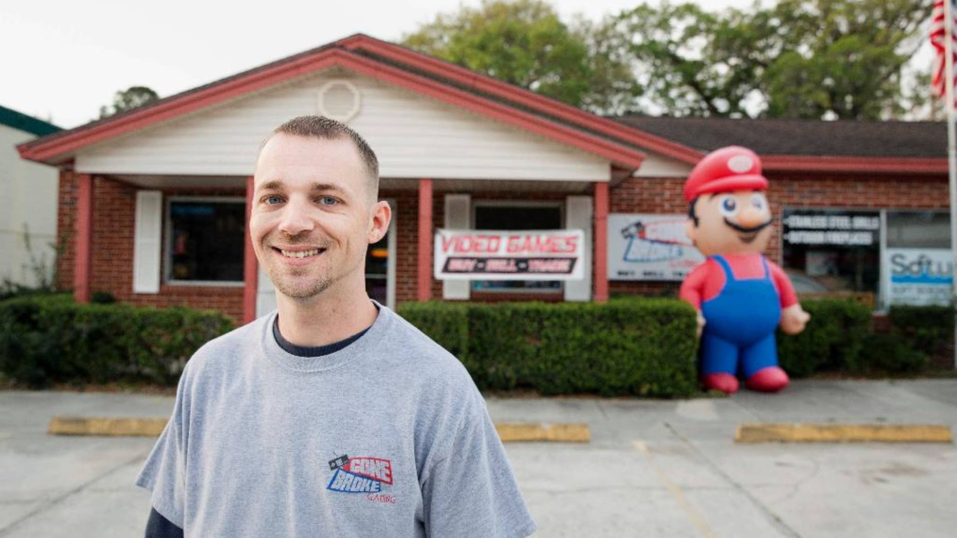 In this undated photo provided by the Institute for Justice, Scott Fisher stands outside his video game store in Orange Park, Fla., a suburb of Jacksonville. A Florida city is saying "game over" to a business owner's decision to inflate a 9-foot-tall (2.7-meter-tall) Super Mario outside his shop. Fisher filed a federal lawsuit on Thursday, April 6, 2017, arguing that the town's ban violates his free speech. (Institute for Justice via AP)