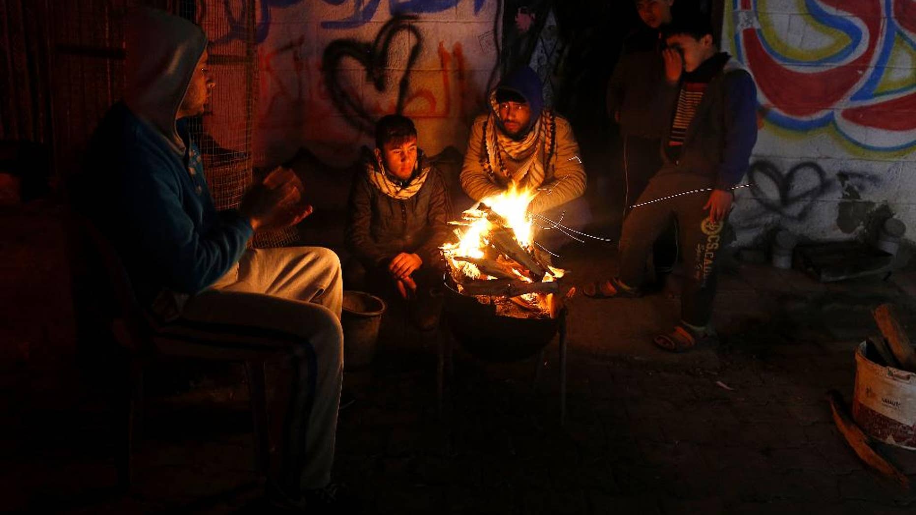 FILE -- In this Jan. 25, 2016 file photo, Palestinians, who get only several hours of electricity a day, sit around a fire outside their home in Gaza City. Israel said Thursday, April 27, 2017, that it was informed that the Palestinian self-rule government in the West Bank will stop paying for electricity Israel sells to the Gaza Strip. Abbas has threatened to exert financial pressure against political rival Hamas to cede control of Gaza, a territory it seized from him in 2007. Gazans now have electricity for only six hours a day. (AP Photo/Hatem Moussa, File)