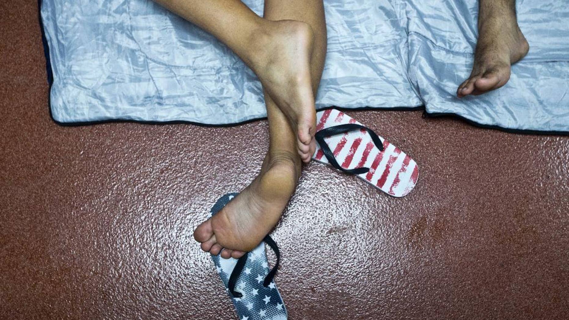 FILE - In this Nov. 21, 2015 file photo, a Cuban migrant's feet rests on a pair of feet flip flops designed with stars and stripes, while resting inside the public restroom of the border control building in Penas Blancas, Costa Rica, border with Nicaragua. New U.S. statistics show nearly twice as many Cuban migrants reached the United States by foot and sea in the last three months of 2015 compared with the same period the year earlier, an exodus apparently fueled by the restoration of diplomatic relations between the former political foes. Department of Homeland Security figures show about 17,000 Cubans reached the United States from October through December. (AP Photo/Esteban Felix, File)