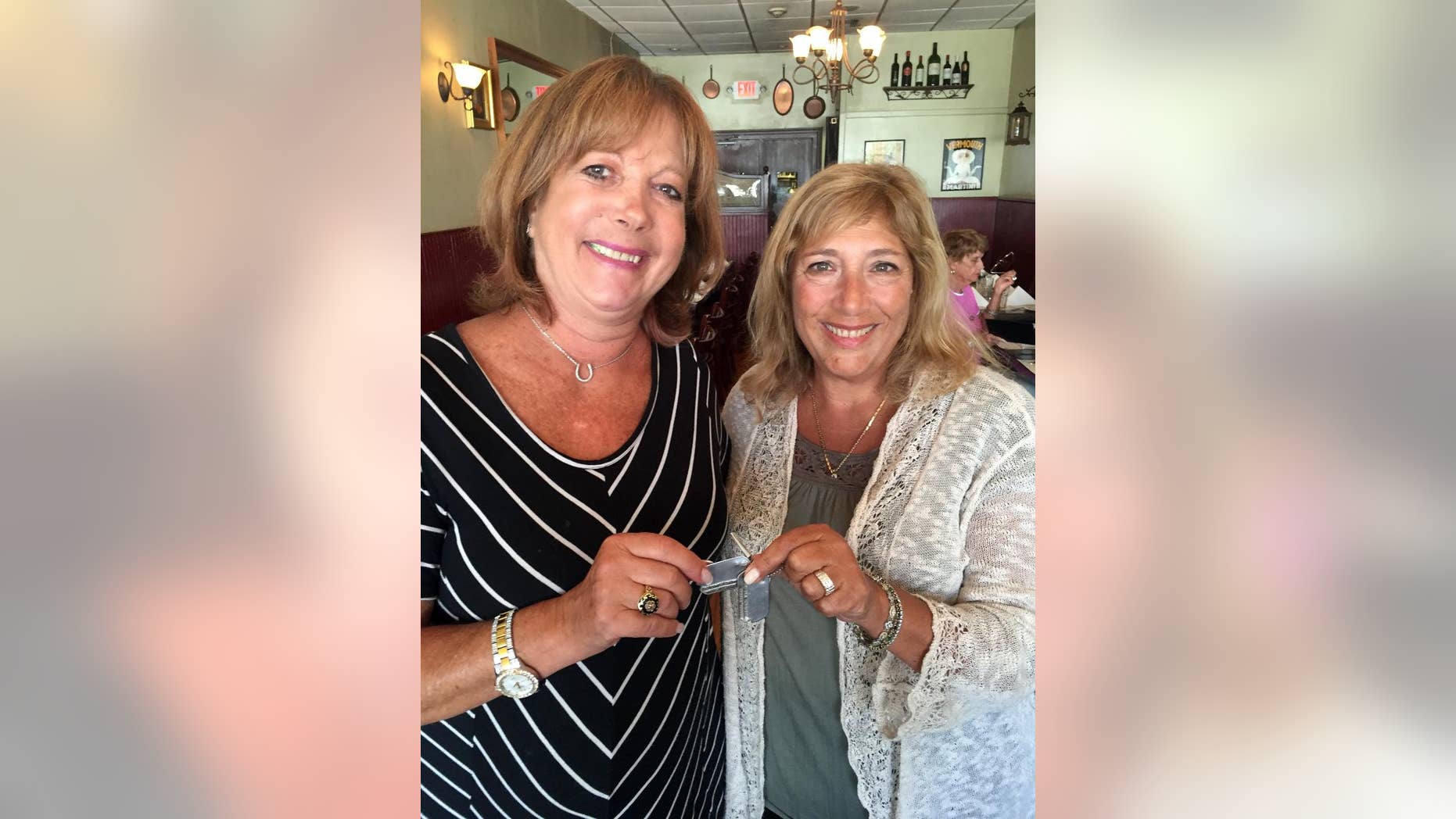 In this photo taken Monday, Aug. 22, 2016 and provided by Audrey Berk, Berk, left, of Queens, N.Y., and Laurie Lubin of Bellmore, N.Y., hold the World War II dog tags of Berk's father, Irving Isaacs in Bellmore, N.Y. Lubin found the tags on a New York City beach in the summer of 1966 and spent the next 50 years trying to return them. Lubin finally tracked down Isaacs' daughter with the help of The Associated Press and gave her the dog tags at a Bellmore restaurant on Aug. 22. (Audrey Berk/Laurie Lubin/Clifford Kaplan via AP)
