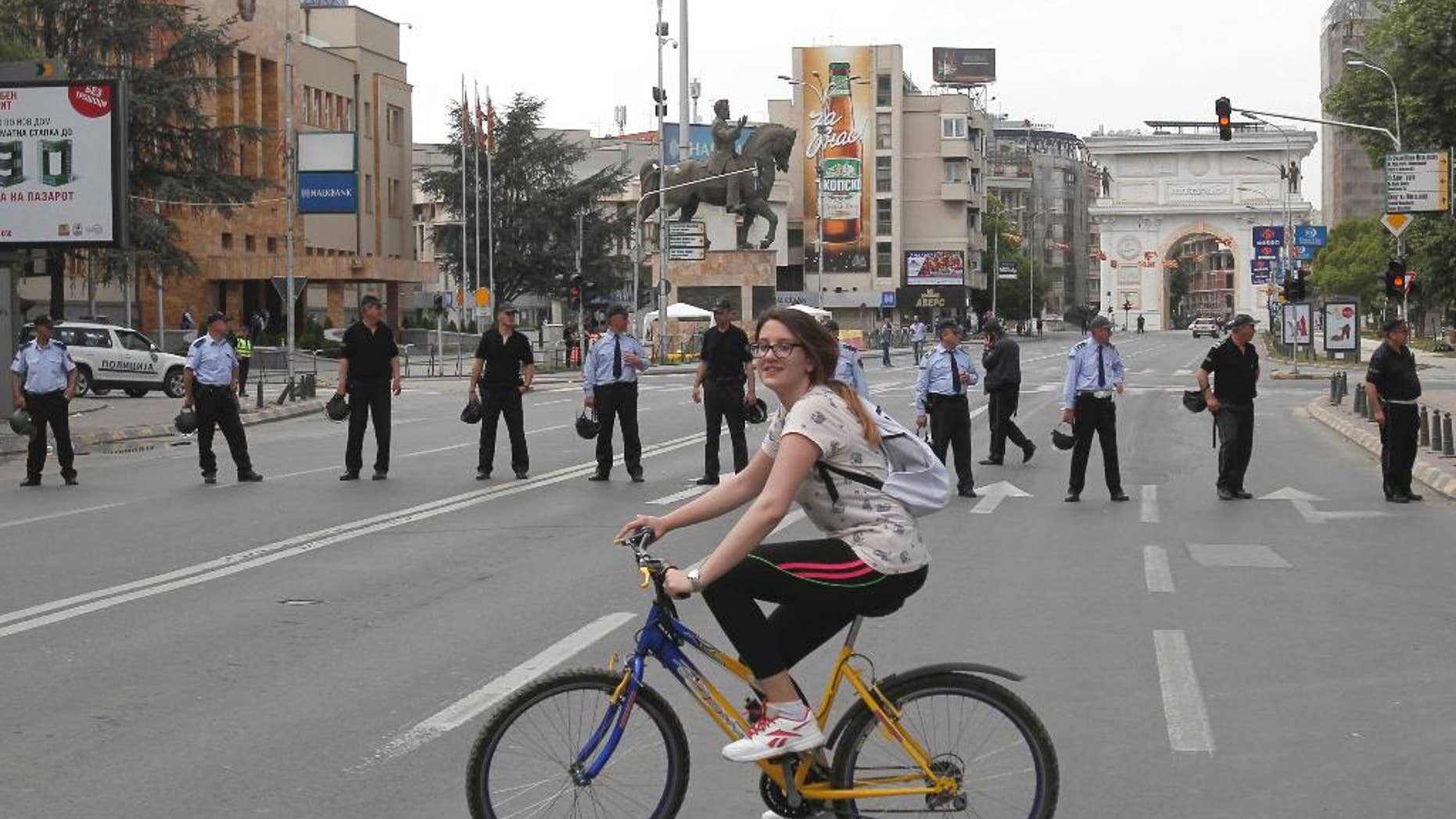 A girl rides a bicycle near a police cordon that blocks the street in front of the parliament building in Skopje, Macedonia, Friday, April 28, 2017. More than 100 people were injured Thursday evening including protestors, policemen and lawmakers, after protesters broke through a police cordon and entered Macedonian parliament to protest the election of a new speaker, despite a months-long deadlock in talks to form a new government. (AP Photo/Boris Grdanoski)