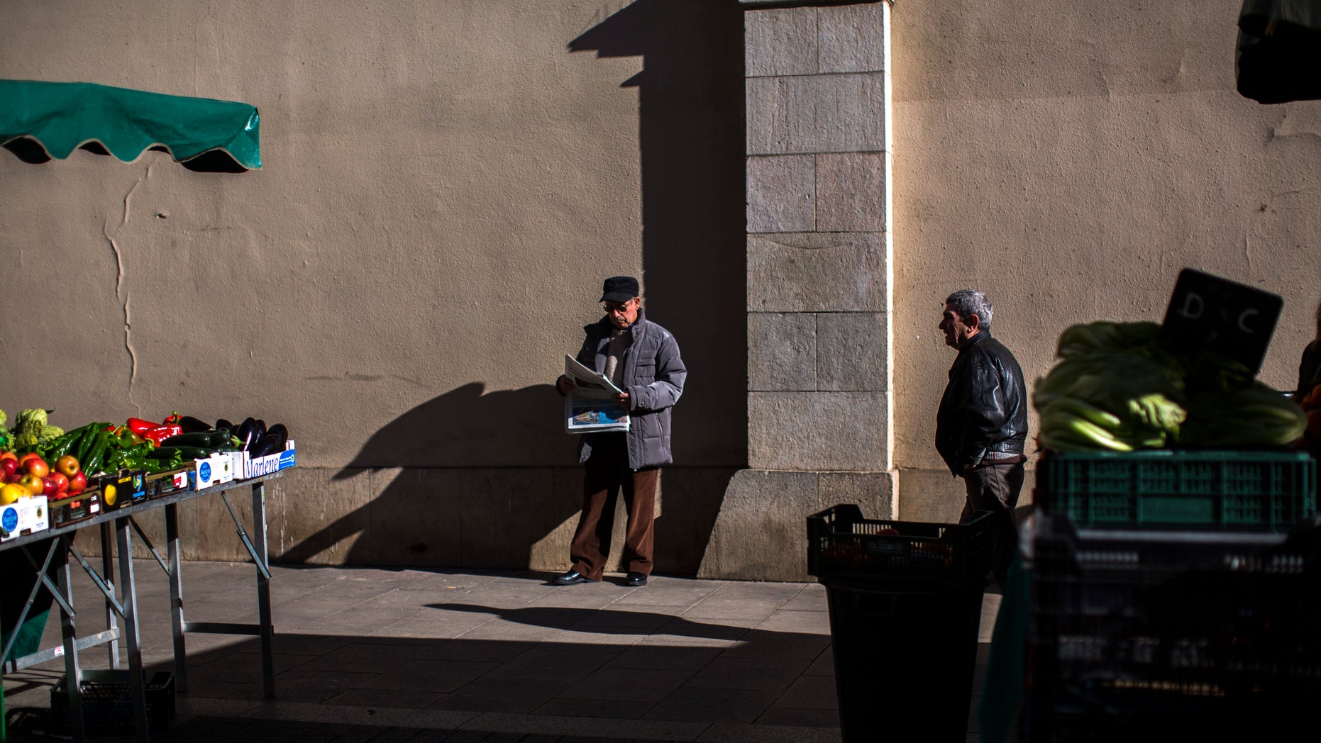 A man reads a newspaper at a fruit market in Barcelona, Spain, Tuesday Jan. 22, 2013. Spain has sold euro 2.8 billion ($3.7 billion) in short-term bills and seen the interest rates it has to pay fall sharply. Spain's borrowing costs have dropped from unsustainable highs last year after the European Central Bank offered to help countries struggling with their debts if they apply for aid. (AP Photo/Emilio Morenatti)