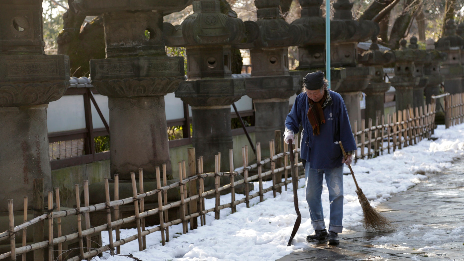 A worker walks away after shoveling snow off a court yard at a temple in Tokyo, Sunday, Feb. 16, 2014. (AP Photo/Shizuo Kambayashi)