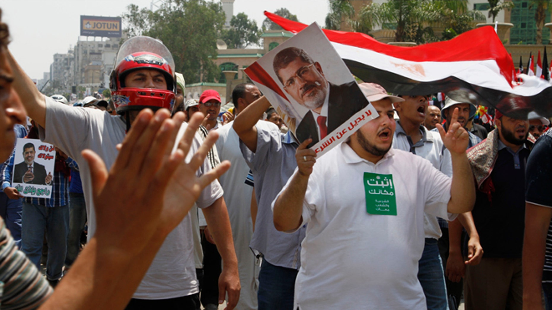 Supporters of Egypt's ousted President Mohammed Morsi wave Egyptian flags and his picture at a sit-in in Nasser City, suburb of Cairo, Egypt, Sunday, July 7, 2013. Egypt's new president moved to assert his authority and regain control of the streets Saturday even as his Islamist opponents declared his powers illegitimate and issued blood oaths to reinstate Mohammed Morsi, whose ouster by the military has led to dueling protests and deadly street battles between rival sides. (AP Photo/Paul Schemm)