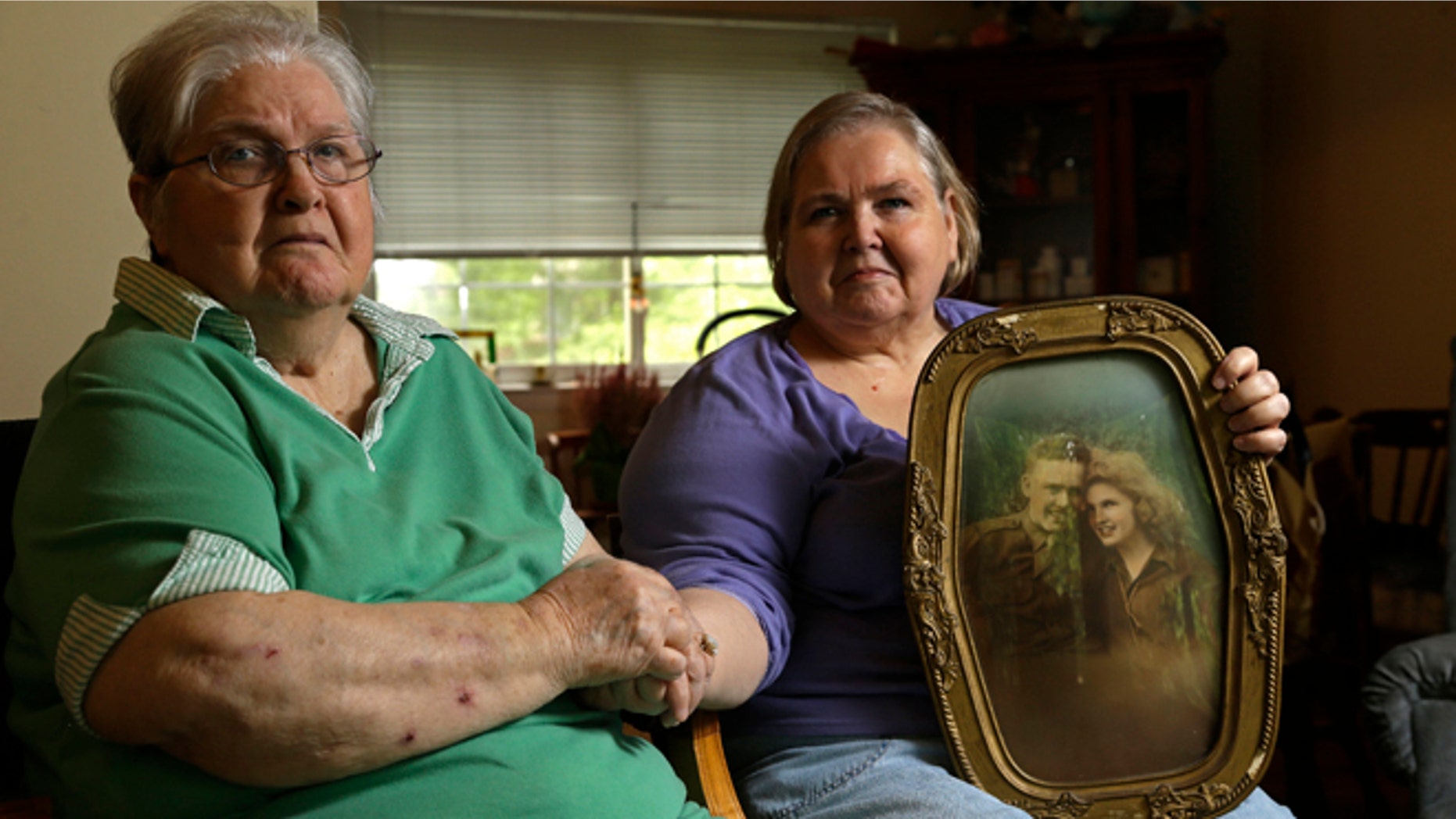 In this photo taken Monday, July 1, 2013 in Chapel Hill, N.C., Shelia Reese, right, sits with her mother Chris Tench holding a portrait of Tench and her father Kenneth F. Reese, a soldier who is still Missing In Action from the Korean War. Tench, who was later remarried, has never known what happened to her husband.