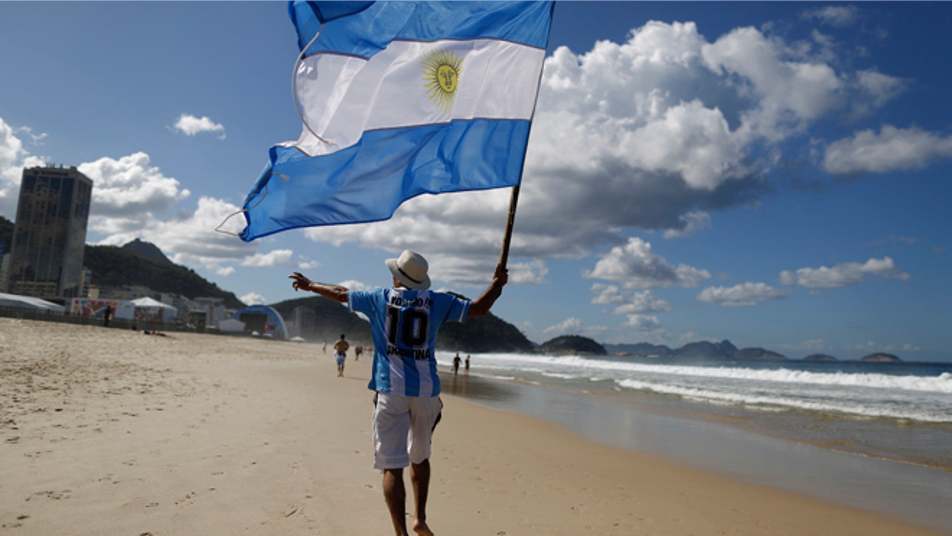 FILE - In this July 14, 2014, file photo, an Argentina soccer fan waves Argentina's national flag the morning after his team was defeated by Germany at the World Cup final, on Copacabana beach in Rio de Janeiro, Brazil. Local media reports say tens of thousands of Argentine fans have remained in the country after the tournament ended. But the prospect of a large number of foreigners selling handicrafts, juggling at intersections for handouts or relying on government social services for poor Brazilians has officials worried. (AP Photo/Leo Correa, File)