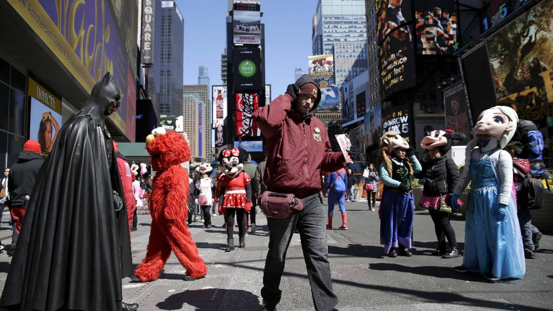 FILE - In this March 29, 2016 file photo, a bus tour ticket seller, center, walks through a group of costumed characters in Times Square in New York. New York City workers have started painting teal rectangles in pedestrian plazas designating where costumed characters can pose with tourists in Times Square. Starting June 21, street performers and costumed characters will be restricted to those areas when soliciting tips from tourists. (AP Photo/Seth Wenig)