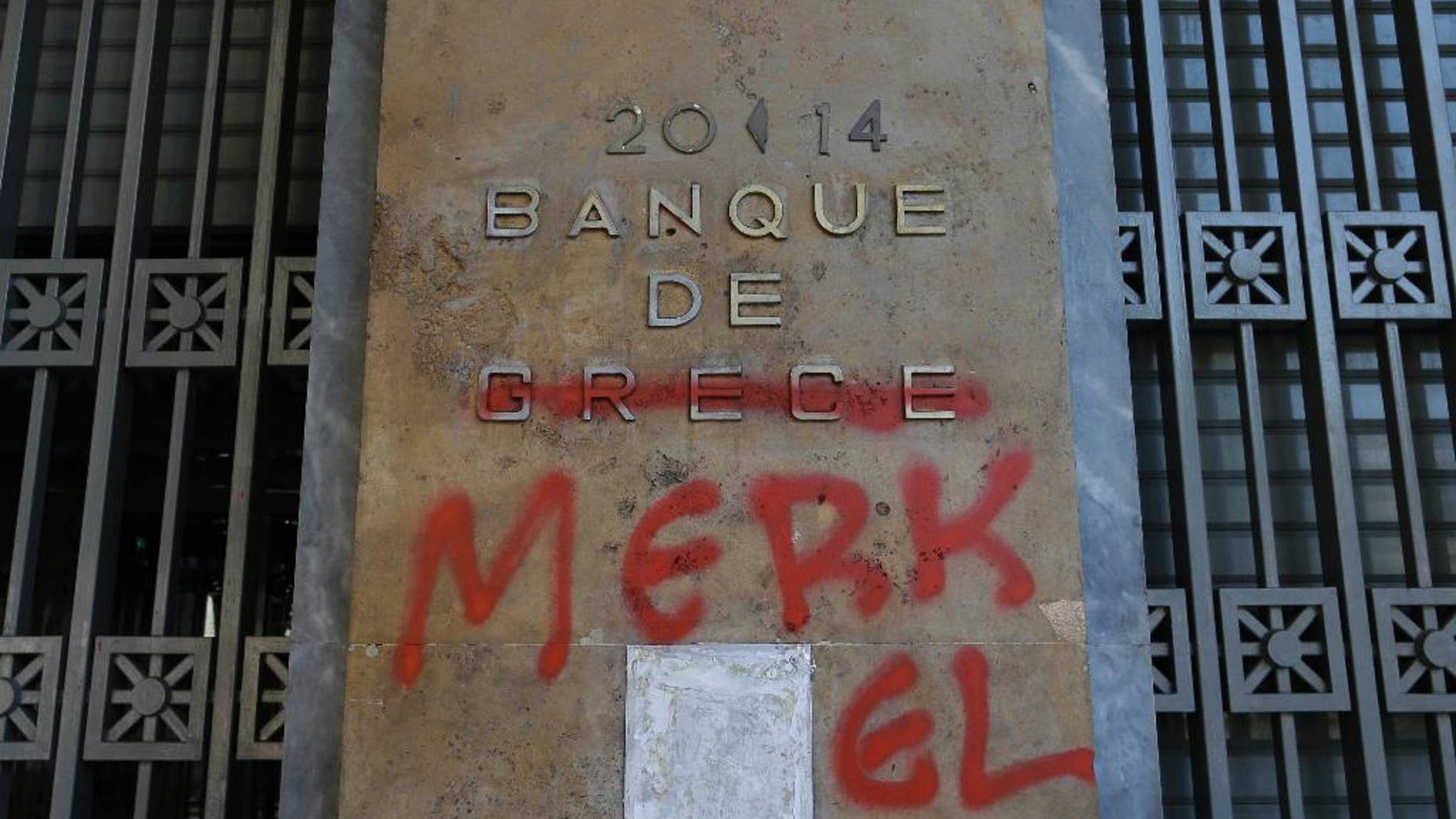 Red spray paint covers a French-language Bank of Greece sign to read 'Bank of Merkel' in reference to German Chancellor Angela Merkel in Athens, Monday, July 6, 2015. Greek Finance Minister Yanis Varoufakis resigned Monday, saying he was told shortly after Greece's decisive referendum result that some other eurozone finance ministers and the country's other creditors would appreciate his not attending the ministers' meetings. (AP Photo/Thanassis Stavrakis)