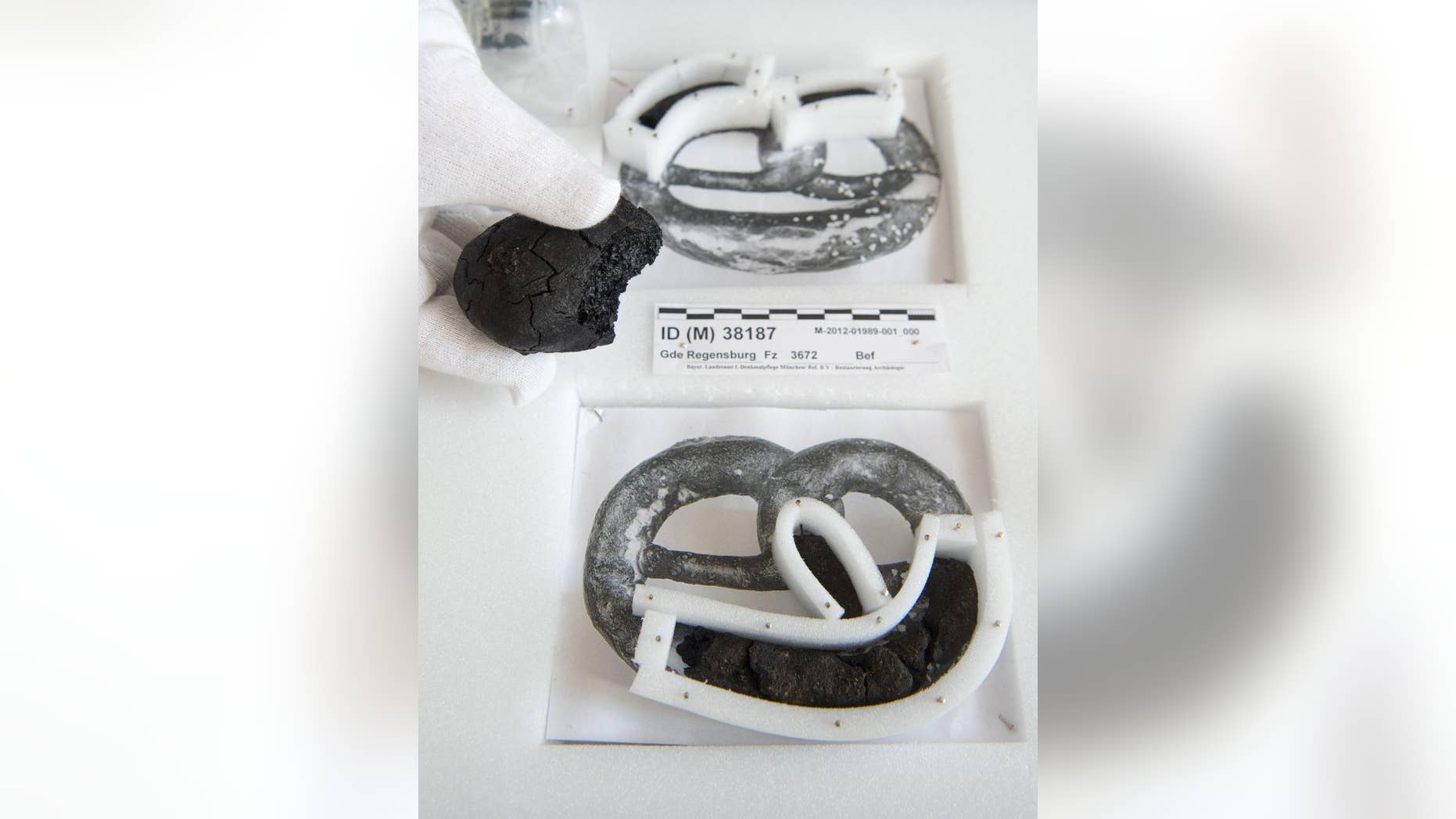 In this March 9, 2015 photo a staff member of the museum presents the remains of 250-year old pretzels and buns at the History Museum in Regensburg. The snacks were found during archeological excavation works. The remains of the pretzel are held by a styrofoam frame placed on a BW photo of a pretzel. (AP Photo/dpa, Armin Weigel)