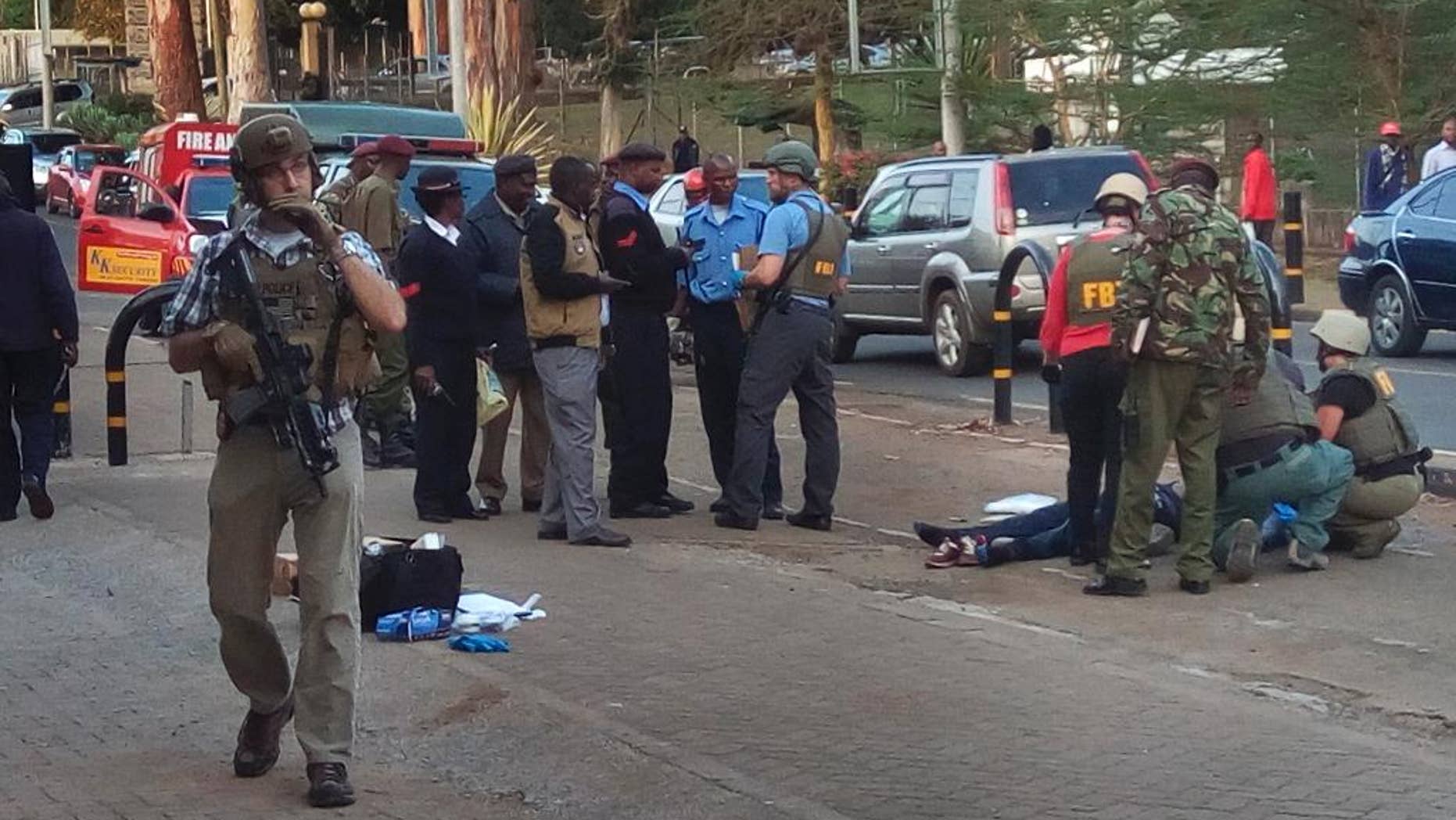 Unidentified U.S. Embassy personnel and Kenyan security forces stand near to the body, right, of a man who was killed outside the U.S. Embassy in Nairobi, Kenya Thursday, Oct. 27, 2016. A Kenyan police official said the man was shot dead after stabbing a policeman guarding the perimeter wall of the U.S. Embassy in Nairobi. (AP Photo/Moses Muoki)