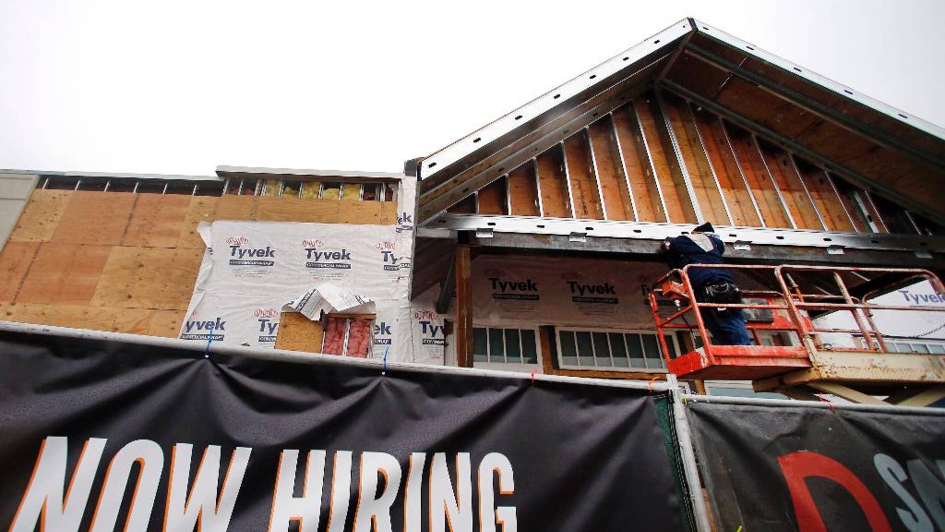 FILE - In this Jan. 12, 2015 file photo, a now hiring sign hangs nearby as a builder works on a commercial property under construction in Peabody, Mass. The Labor Department reports on state unemployment rates for December on Tuesday, Jan. 27, 2015. (AP Photo/Elise Amendola, File)