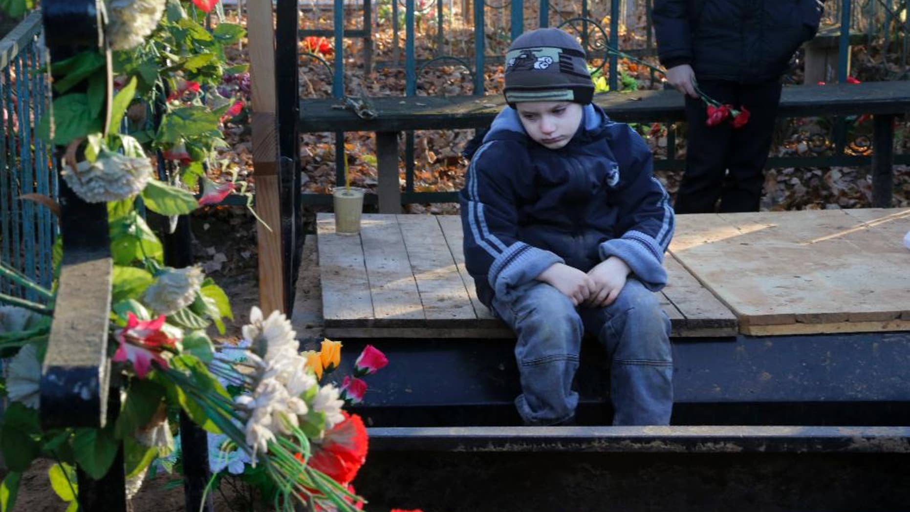 Mikhail, the grandson of one of the plane crash victims Nina Lushchenko, sits at her grave, during her funeral at a cemetery in the village of Sitnya, 80 km (about 50 miles) of Veliky Novgorod, Russia, Thursday, Nov. 5, 2015. The first victim of Saturday's plane crash in Egypt was laid to rest on Thursday following a funeral service in a medieval church in the north Russian city of Veliky Novgorod. Russia's Airbus 321-200 broke up over the Sinai Peninsula en route from the resort town of Sharm el-Sheikh to St. Petersburg, killing all 224 on board. (AP Photo/Dmitry Lovetsky)