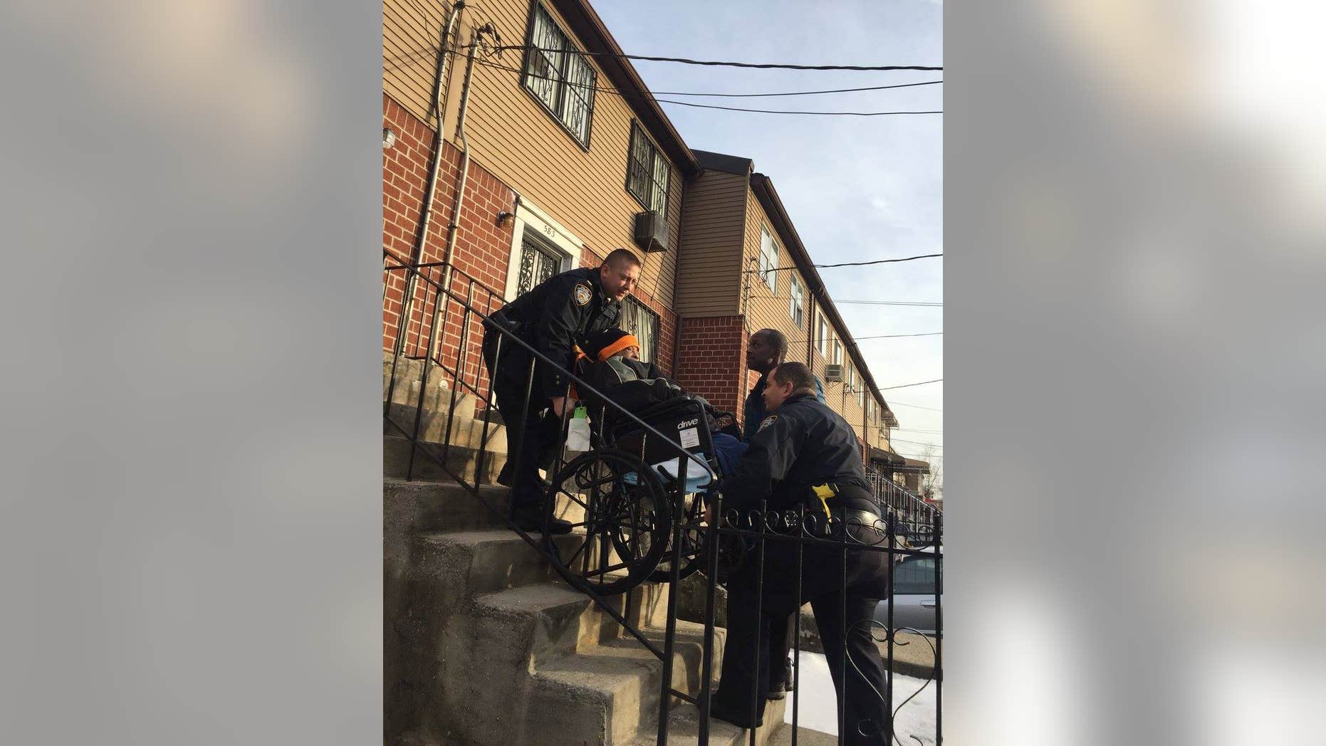 NYPD Officers Vitaliy Zelikov and Georin Duran work together to carry a wheelchair-bound 85-year-old man up the stairs.