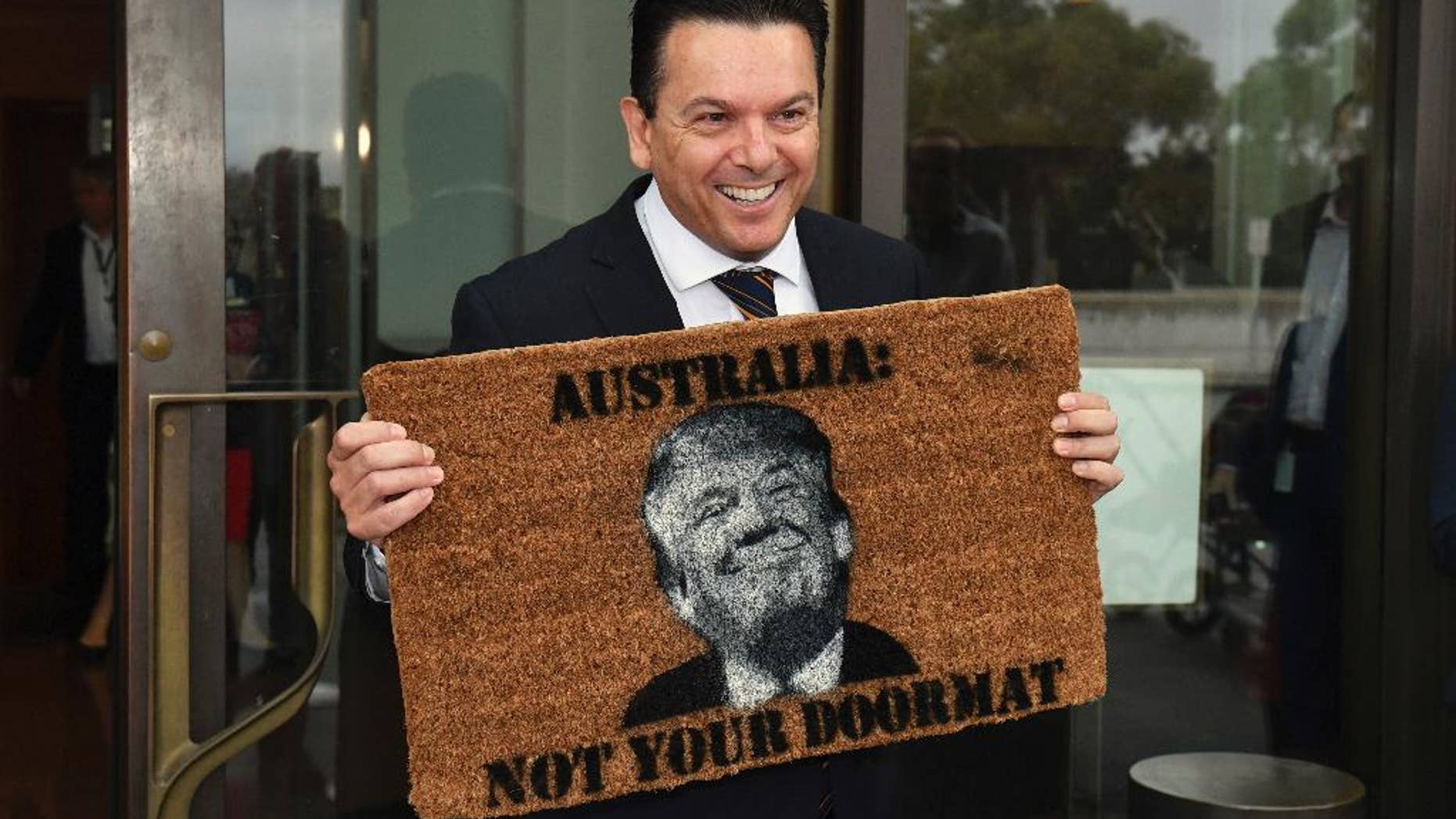 Australian Senator Nick Xenophon arrives at the Senate entrance at Parliament House in Canberra, holding a doormat featuring an image of United States President Donald Trump, Tuesday, Feb. 7, 2017. (Mick Tsikas/AAP Image via AP)