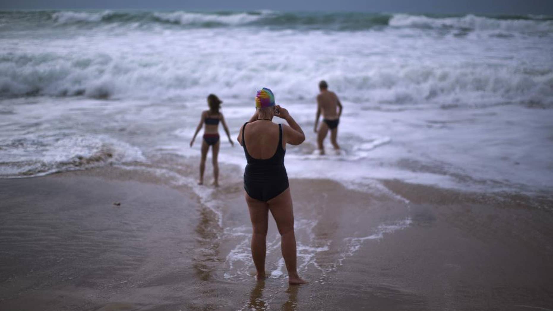 FILE- In this Jan. 1, 2014 file photo, German tourists walk on the seashore as one of them takes a photograph, after swimming in the Atlantic ocean in a beach in Cadiz, southwest Spain. Nudists have lost a seven-year legal battle for access to a popular tourist resort beach on Spain's southwestern tip. (AP Photo/Emilio Morenatti, File)