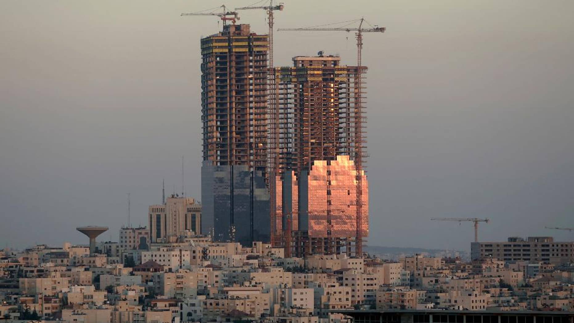 FILE -- In this Sunday, July 6. 2008 file photo, the sunset reflects on the Jordan Gate Towers under construction in Amman, Jordan. Murad Awamleh, a senior official in the Amman municipality, said Monday, May 23, 2016 that work will resume on the half-built twin towers that have blighted the skyline of the Jordanian capital for years, a symbol of mega construction schemes gone awry. The official said the Gulf-based Al Bayan Holding Company, and a Jordanian firm, Al Hamad Contracting, reached a deal to complete the Jordan Gate Towers within two years for $120 million. (AP Photo/Nader Daoud, File)
