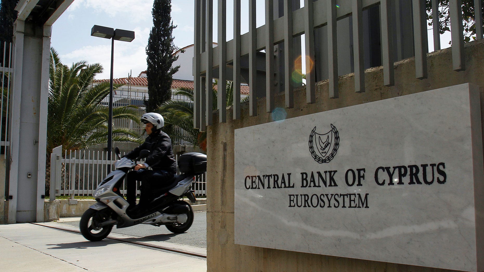 FILE - The March 13, 2012 file photo shows a man on a scooter, exiting from a gate of Central Bank of Cyprus in Nicosia, Cyprus. When it came to helping out Greece, Ireland and Portugal, Germany grudgingly went along with its European partners and backed hundreds of billions in rescue loans. But now that tiny Cyprus is in trouble, German politicians for the first time appear in no mood to help _ which could put the Mediterranean island country on the path to bankruptcy and out of the eurozone. (AP Photo/Petros Karadjias)