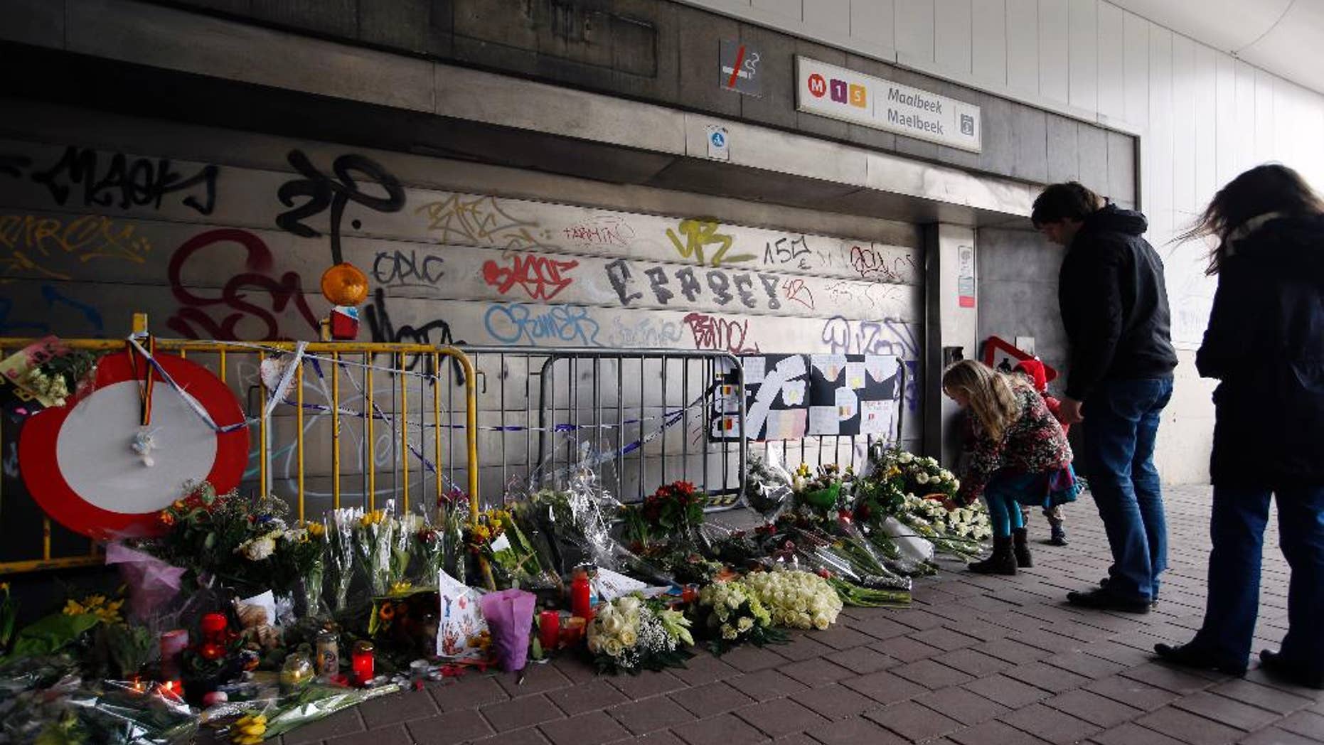 FILE - In this Saturday, March 26, 2016 file photo, people stop and look at floral tributes placed outside the Maelbeek metro station, the scene of one of the bomb attacks on the Belgian capital, in Brussels. The subway station in the Belgian capital where a suicide bomber killed 16 people a month ago will reopen Monday, April 25, 2016. The Brussels regional transit authority, commonly known as the STIB, announced the reopening Friday, April 22 on social media. (AP Photo/Alastair Grant, file)