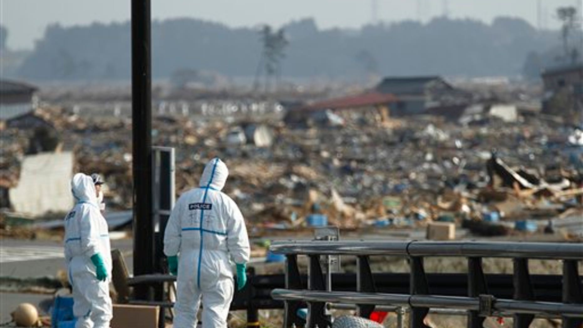April 15: Japanese police officers stand by bodies of victims while searching for missing people at a devastated area in Namie of Fukushima Prefecture, northeastern Japan. In the background is part of the Fukushima Dai-ichi nuclear complex. (AP)