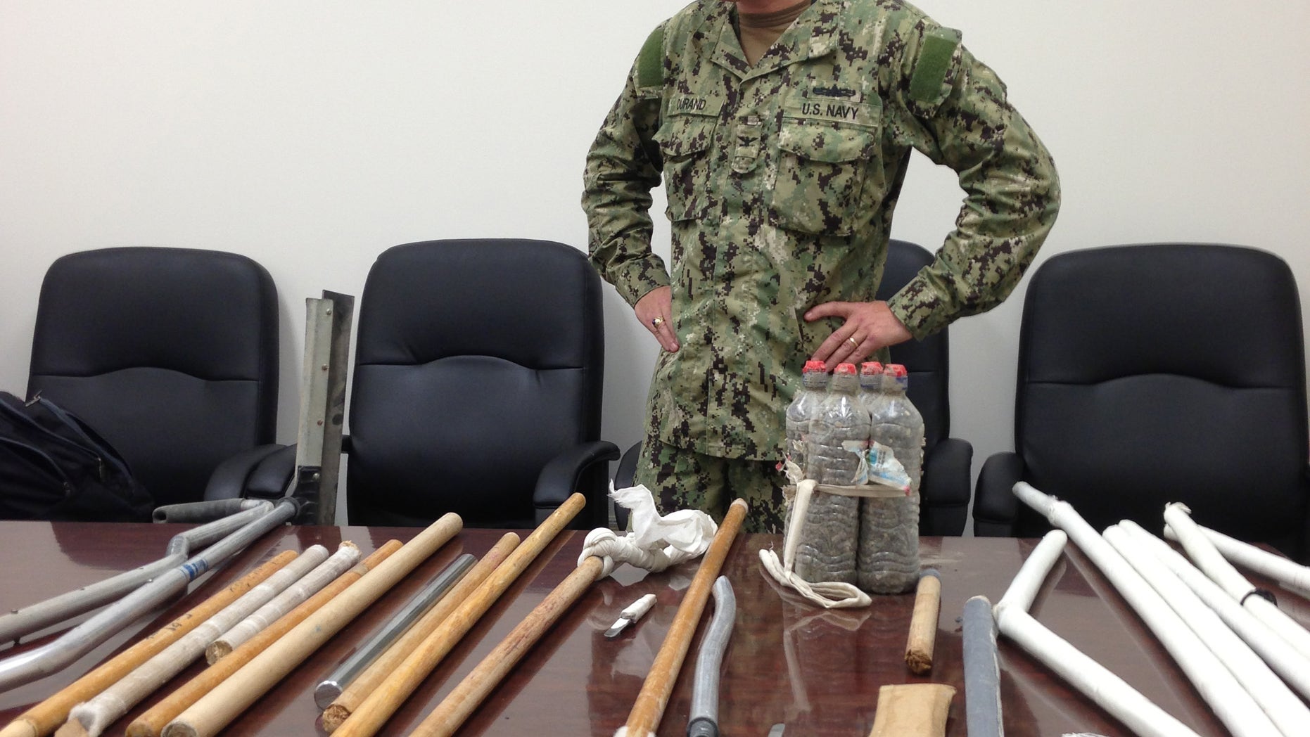 In this image reviewed by the U.S. Military, Navy Capt. Robert Durand stands next to some of the makeshift weapons, including broomsticks and batons made of plastic and steel, that were confiscated from prisoners at the Guantanamo Bay prison following a Saturday clash between prisoners and guards, on display for the press at the U.S. Naval Base Guantanamo Bay in Cuba, Tuesday, April 16, 2013. Soldiers with riot helmets and shields swept into recreation yards and met with resistance from several dozen prisoners, the leadership of the detention center said. The guard force raided Camp 6 because the prisoners had for several weeks covered up 147 of the 160 security cameras, making it impossible to monitor them amid a weeks long hunger strike. The hunger strike goes on, with 45 prisoners refusing meals and 13 being force fed, officials said. (AP Photo/Ben Fox)