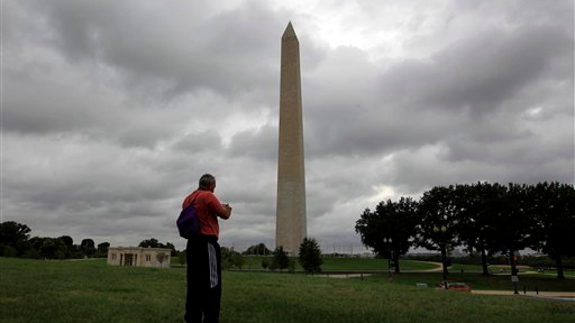 A tourist takes a picture of the recently damaged Washington Monument as clouds from Hurricane Irene moves up the Eastern Seaboard towards Washington, Saturday, Aug. 27, 2011. The monument has been closed to the public it was damaged in the earthquake that shook the capital last Tuesday. (AP Photo/Luis M. Alvarez)