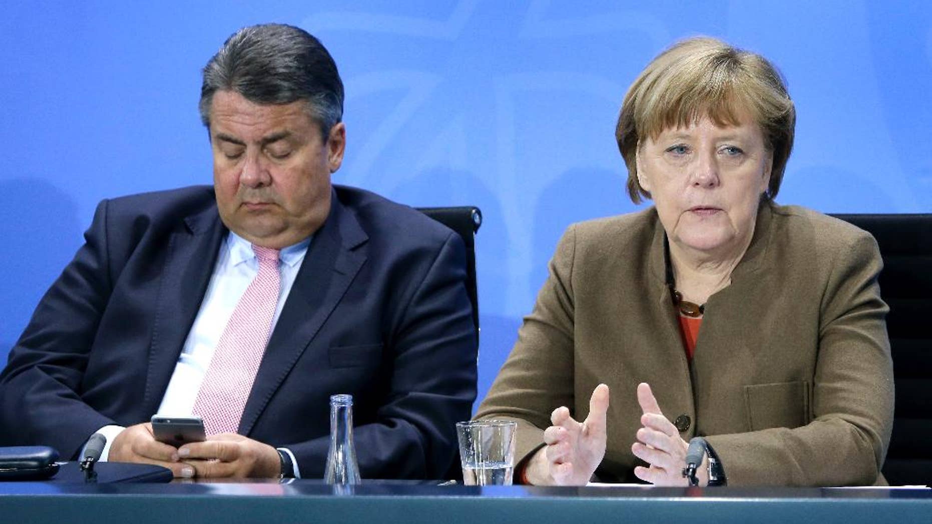 Sigmar Gabriel, left, Chairman of the German Social Democrats, looks at his smartphone as German Chancellor Angela Merkel, right, speaks during a press conference in Berlin, Germany, Thursday, April 14, 2016 on the results of a meeting of the heads of the German government coalition. (AP Photo/Michael Sohn)