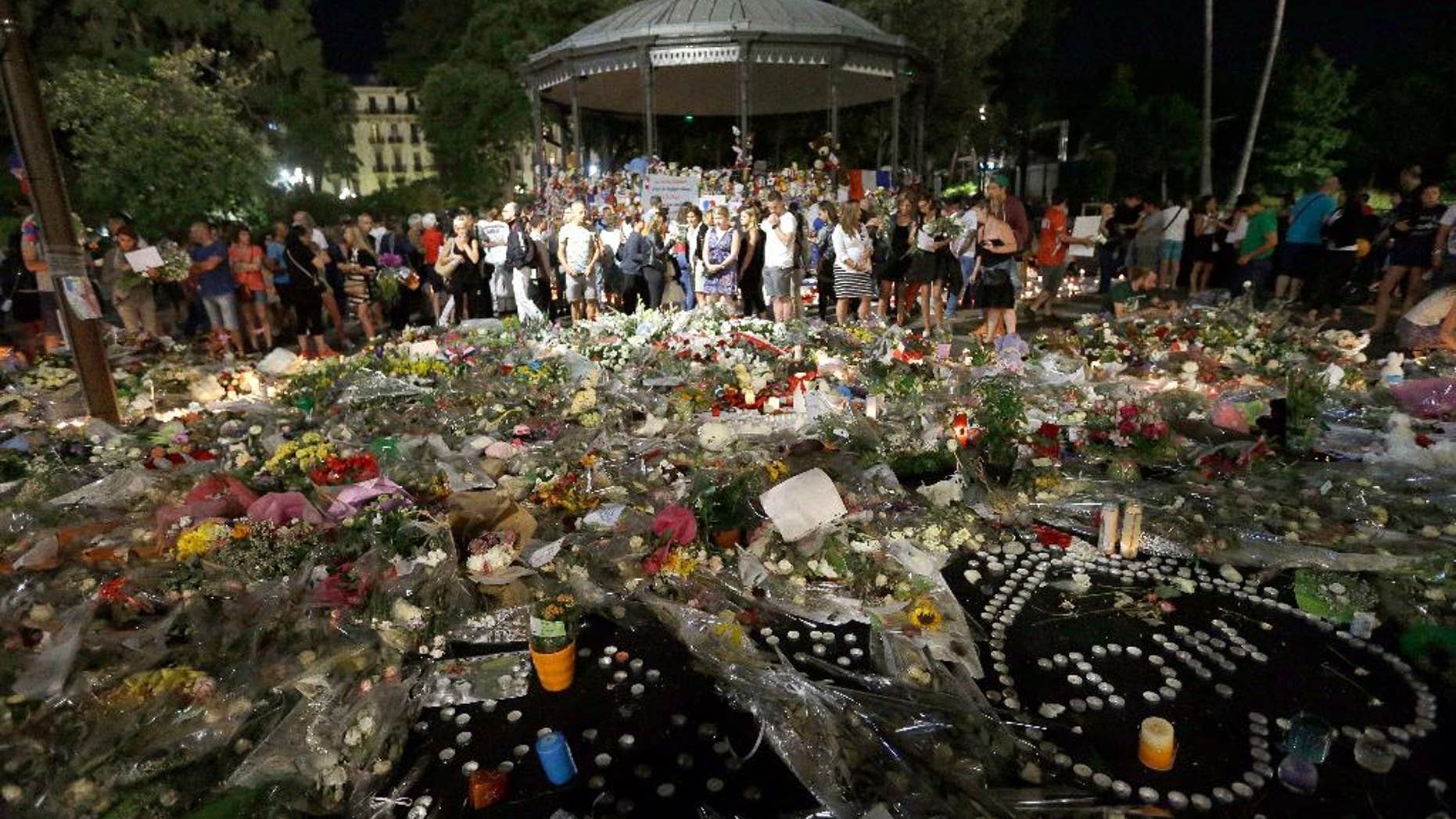 People gather in a new memorial in a gazebo in a seaside park on the famed Promenade des Anglais in Nice, southern France, Monday, July 18, 2016. Mourners formed a human chain to remove flowers, candles and other mementos placed along the Promenade des Anglais as spontaneous memorials to the victims of the Bastille Day attack in preparation to open the westbound lane.(AP Photo/Claude Paris)
