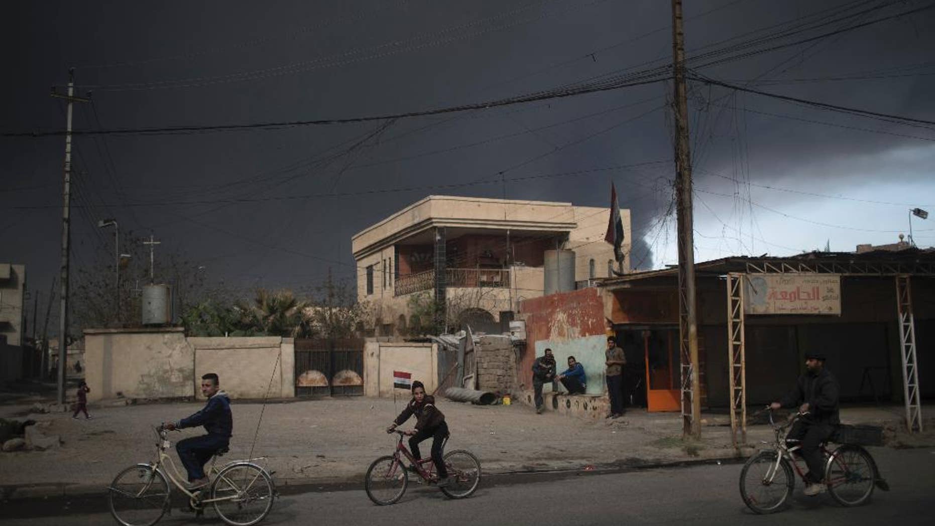 FILE - In this Sunday, Nov. 6, 2016, a boy, center, rides his bike with an Iraqi flag, in Qayara, south of Mosul, Iraq, . When Iraqi forces drove Islamic State militants from the town of Qayara in August, it was hailed as an early triumph over the extremists. But the government has failed to restore lost services, violent revenge attacks persist, and some residents are bitter and angry. (AP Photo/Felipe Dana, File)