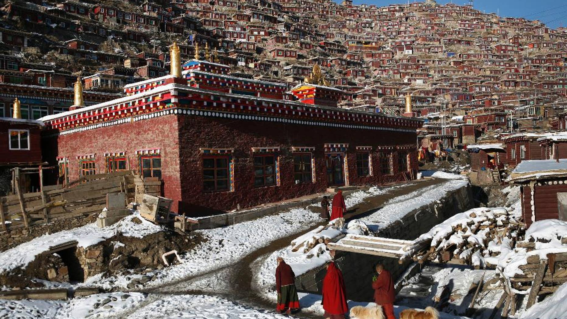 FILE - In this Nov. 23, 2009, file photo, Tibetan nuns walk near houses and monastery built on the mountain also known as Sertar Buddhist Institution or Larung Gar in Sertar county, southwest China's Sichuan province. China says it is rebuilding the major center of Buddhist learning in the country's west, following reports last year that the complex was being demolished and its residents evicted. An official and state media on Tuesday, March 14, 2017 said the project aims to eliminate dangers to safety and health at Larung Gar, which had been home to thousands of monks, nuns and laypeople studying the religion. (Chinatopix via AP, File)