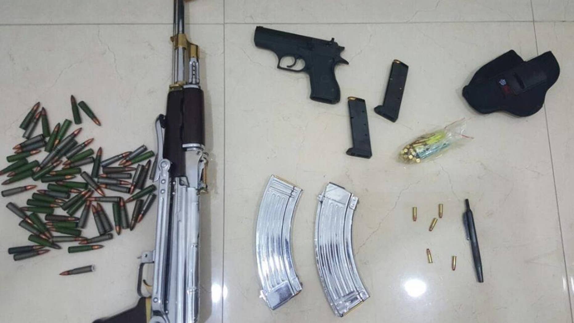 In this Tuesday, June 14, 2016 photo released by the Kuwait Ministry of Interiors, a Kalashnikov rifle, a handgun and ammunition plus a pen gun found and presented after authorities raided the home of Sheikh Athbi al-Fahad Al Sabah the former head of Kuwait's National Security Office, in Kuwait. The hunt for a renegade nephew of Kuwait's emir has turned up a gun disguised as a pen in his home, adding yet another layer of mystery to a bizarre case involving two other ruling family members and others.( Kuwait Ministry of Interiors via AP)