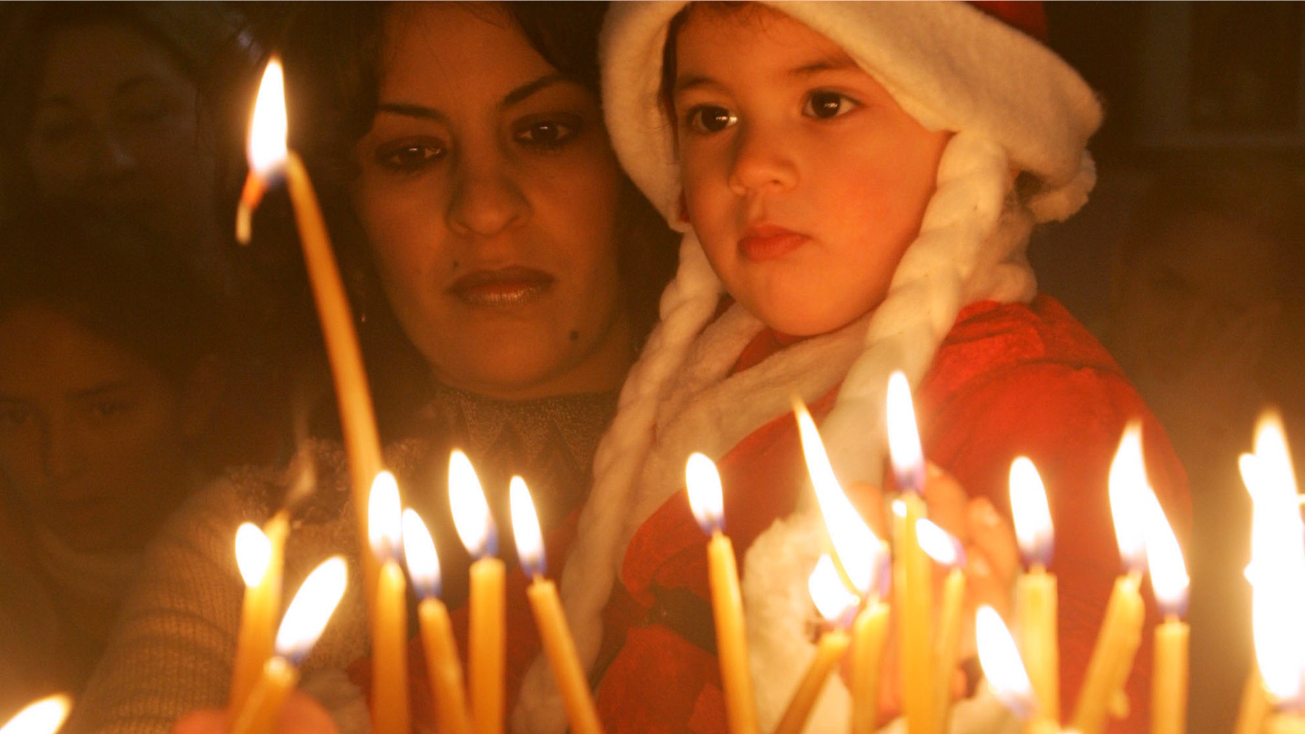 BETHLEHEM, WEST BANK - DECEMBER 24: Iman Haddid and her 2-year-old daughter Dallah light votive candles at the Church of the Nativity December 24, 2004 in the biblical town of Bethlehem in the West Bank. A smaller crowd than in prevous years gathered in Manger Square for the start of the Christmas festivities at the traditional birthplace of Jesus with the local Palestinian governor blaming Israel for not easing security restrictions in time. (Photo by David Silverman/Getty Images)