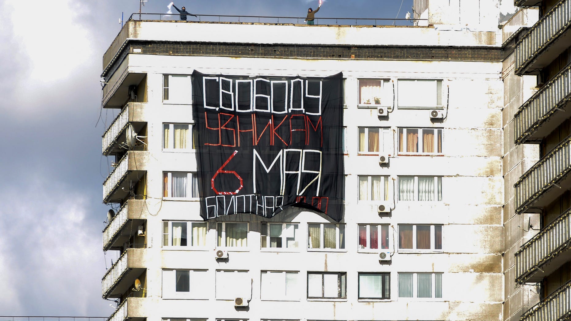 Two opposition activists hold flyers as they unfurl a banner that reads: "Freedom of prisoners on May 6!" in support of opposition activists who were arrested at last year's May 6 rally on Bolotnaya Square (Swamp) Square on a building in New Arbat street in Moscow, Russia, May 6, 2013, ahead of a massive planned rally Monday afternoon. (AP Photo/Mitya Aleshkovskiy)