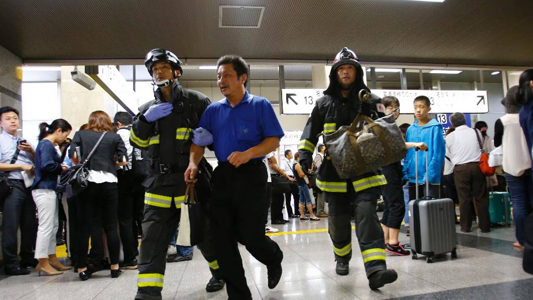 A passenger is escorted by firefighters after getting off a high-speed bullet train where a man set himself of fire, at Odawara station in Odawara, west of Tokyo, Tuesday, June 30, 2015. The man riding one of Japan's high-speed bullet trains set himself on fire Tuesday, killing himself as the coach filled with smoke, Japanese officials and media reports said. (AP Photo/Shizuo Kambayashi)