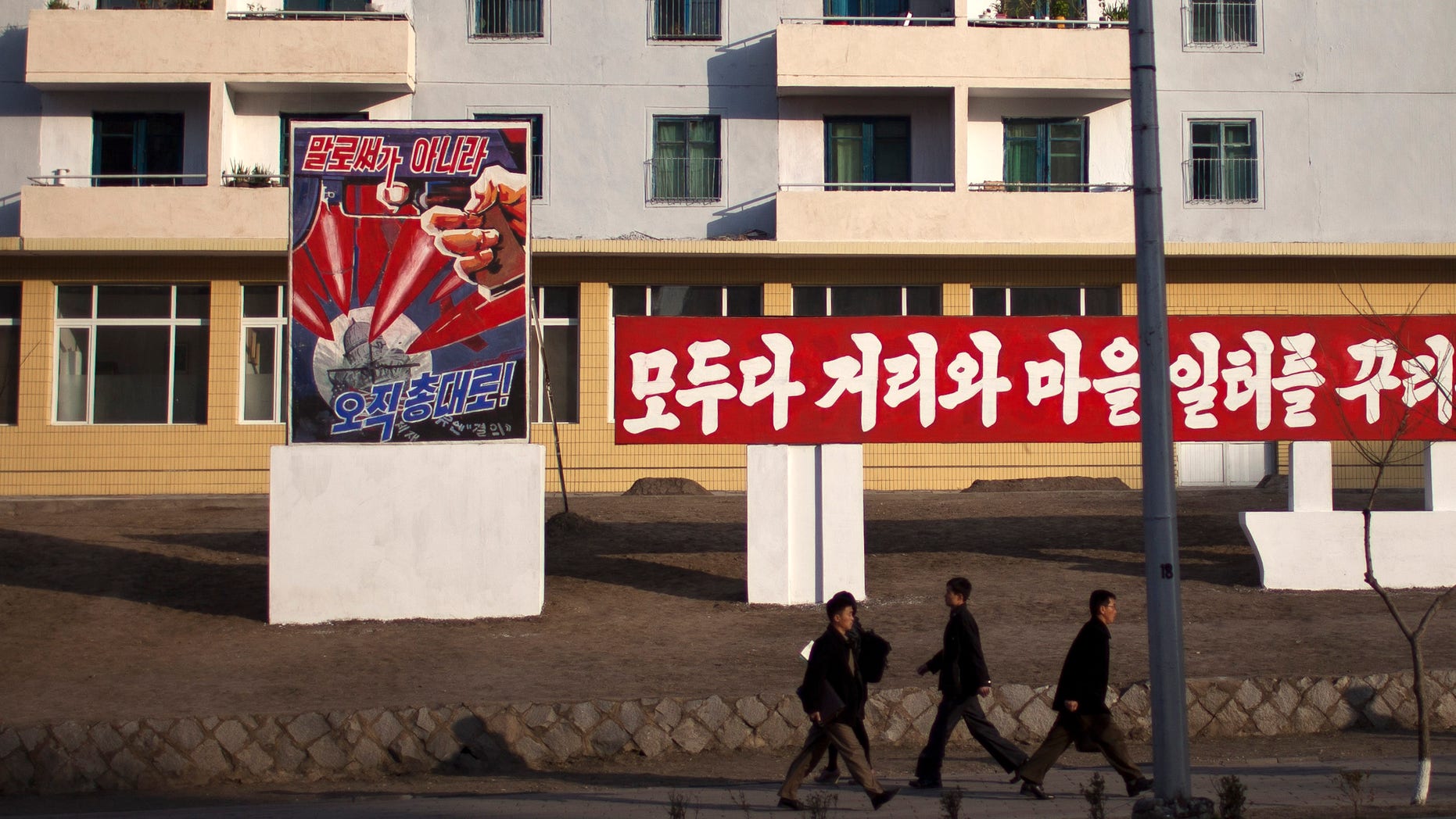 ADDS THE TRANSLATION OF THE POSTER - Morning commuters walk past a poster showing weapons targeting the White House building on a street in Pyongyang, North Korea, Friday, April 19, 2013. The poster reads: "Not by words, but only through arms" (AP Photo/Alexander F. Yuan)