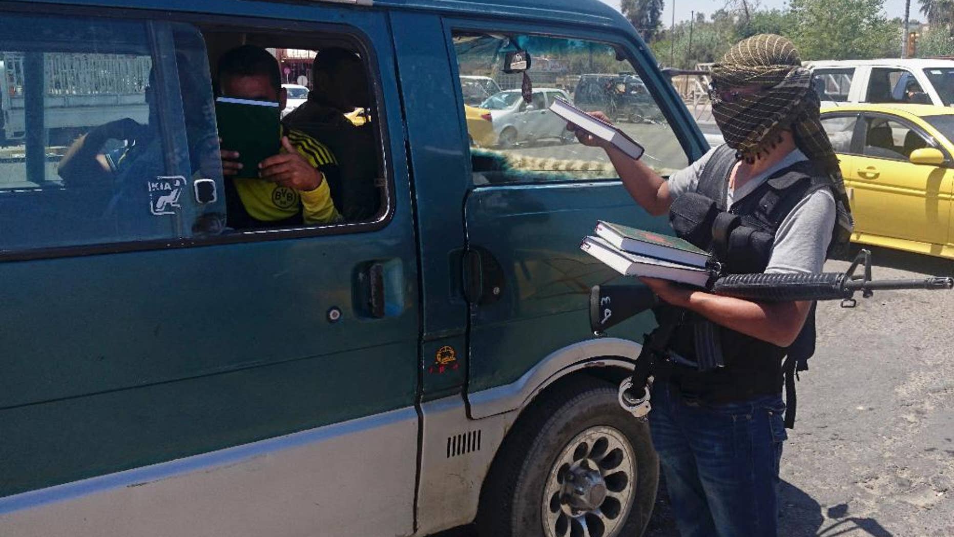 FILE - In this Sunday, June 22, 2014 file photo, a fighter from the militant group who refer to themselves as the Islamic State, distributes a copy of the Quran, Islam's holy book, to a driver in Mosul, 225 miles (360 kilometers) northwest of Baghdad, Iraq. The extremist-held Iraqi city of Mosul is set to usher in a new school year. But unlike years past, there will be no art or music, and classes about history, literature and Christianity have been “permanently annulled.” (AP Photo, File)