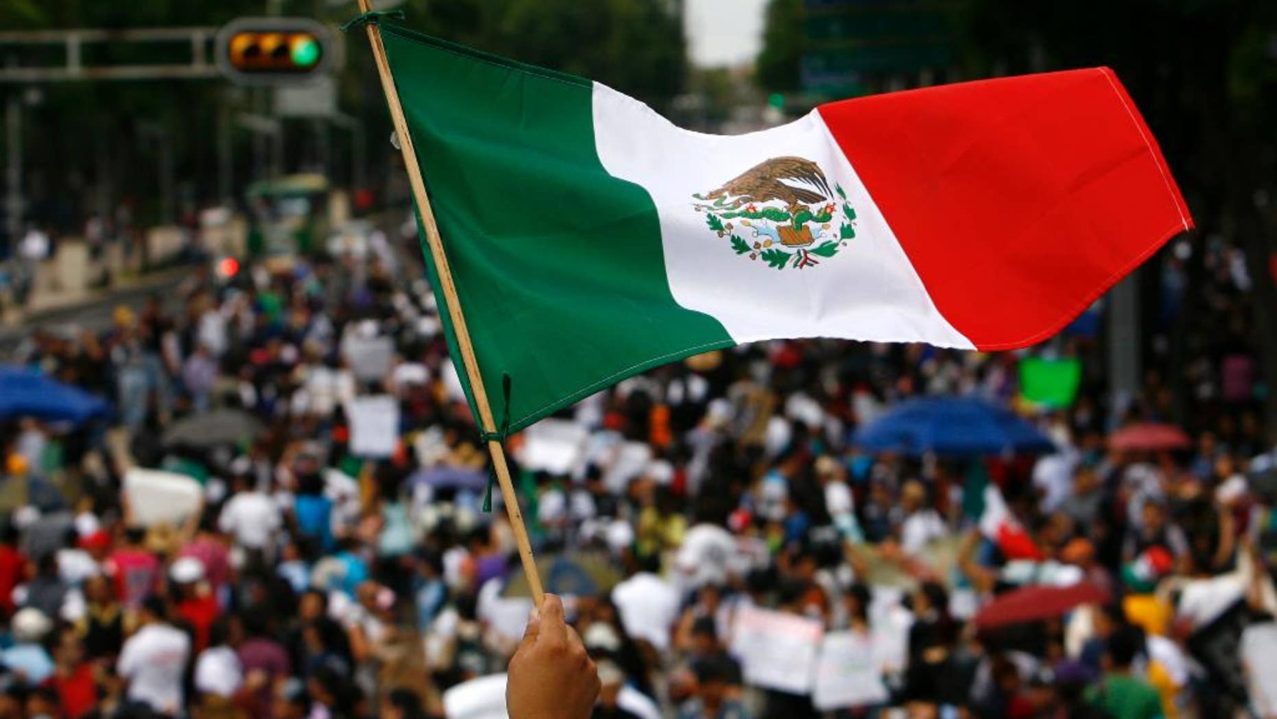 FILE - In this July 7, 2012 file photo, a woman waves a national flag as Mexicans march along Avenida Reforma on their way to Mexico City's main plaza, the Zocalo. The results of the last polls to be released before the Sunday, June 7, 2015 midterm elections show Mexico’s ruling party appears poised to retain its leading position in congress, but may lose the ability to cobble together a majority with smaller parties. (AP Photo/Marco Ugarte, File)