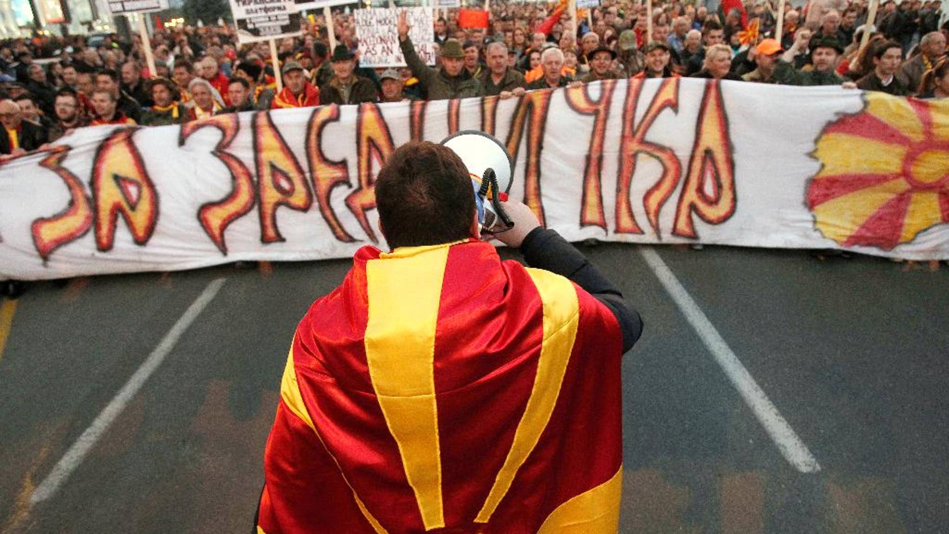 A man wrapped in a Macedonian flag leads a protest march through a street in Skopje, Macedonia, Thursday, March 16, 2017. Thousands of Macedonians protested peacefully for a third week in the capital Skopje and other cities, against the designation of Albanian as a second official language nationwide. The banner reads in Macedonian "For Common Macedonia". (AP Photo/Boris Grdanoski)