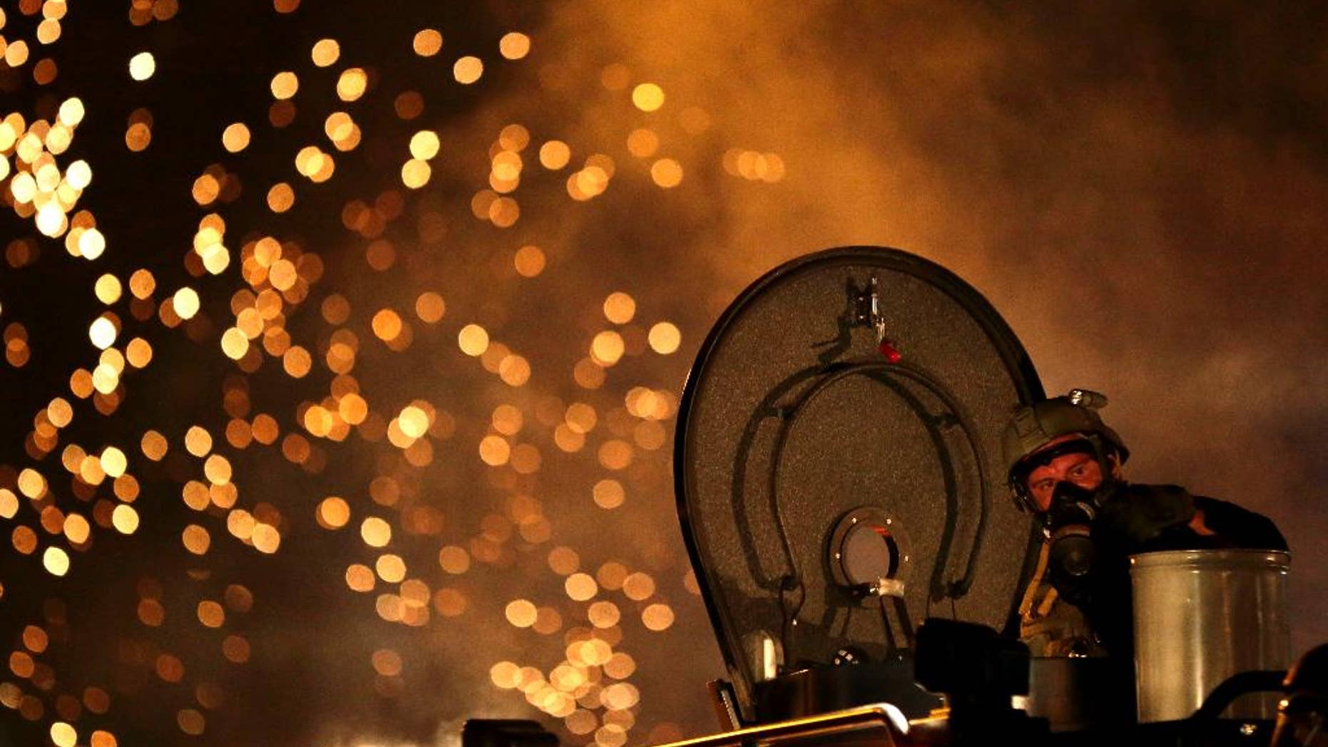 FILE - In this Aug. 17, 2014 file photo, a law enforcement officer watches from an armored vehicle after a device was fired to disperse a crowd during a protest for Michael Brown, in Ferguson, Mo. Law enforcement officials have lobbied to protect federal programs that have funneled billions of dollars in high-powered weapons and other military-style equipment to state and local police forces, calling the equipment critical in this era of terror threats and the all-too-frequent mass shootings that demand a swift and effective response. (AP Photo/Charlie Riedel, File)