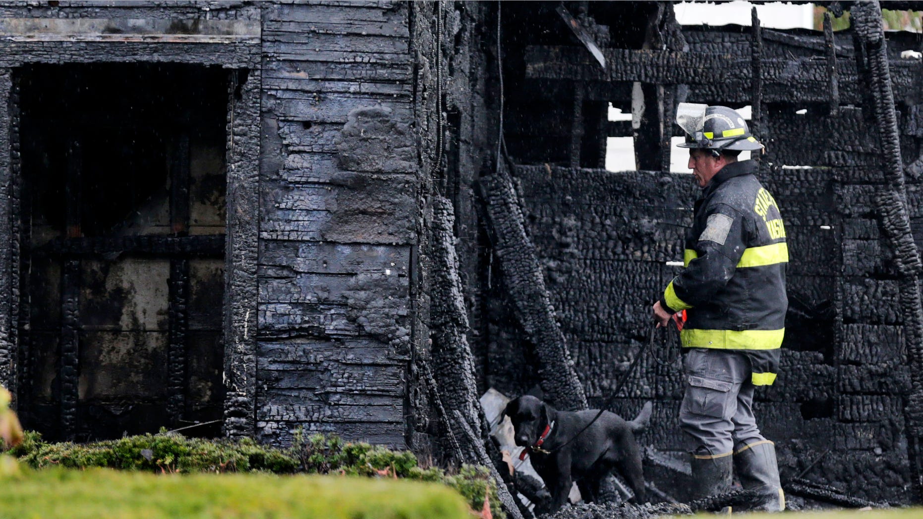 An arson detection dog and investigator from the State Fire Marshal's office search through debris after an apartment fire in Lawrence, Mass., Tuesday, Oct. 21, 2014. Two children died in the blaze. (AP Photo/Charles Krupa)