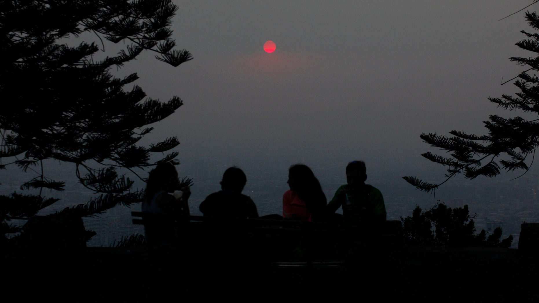 A group of people relax on a park bench at Cerro San Cristobal Park overlooking the Chilean capital which is shrouded by a cloud of smoke from dozens of forest fires that burn near Santiago, Chile, Wednesday Jan. 8, 2014. Residents of Santiago have been suffering from high levels of air pollution caused by the fast-spreading forest fires. The blazes that started over the weekend have caused more than $100 million in property losses. (AP Photo / Luis Hidalgo).