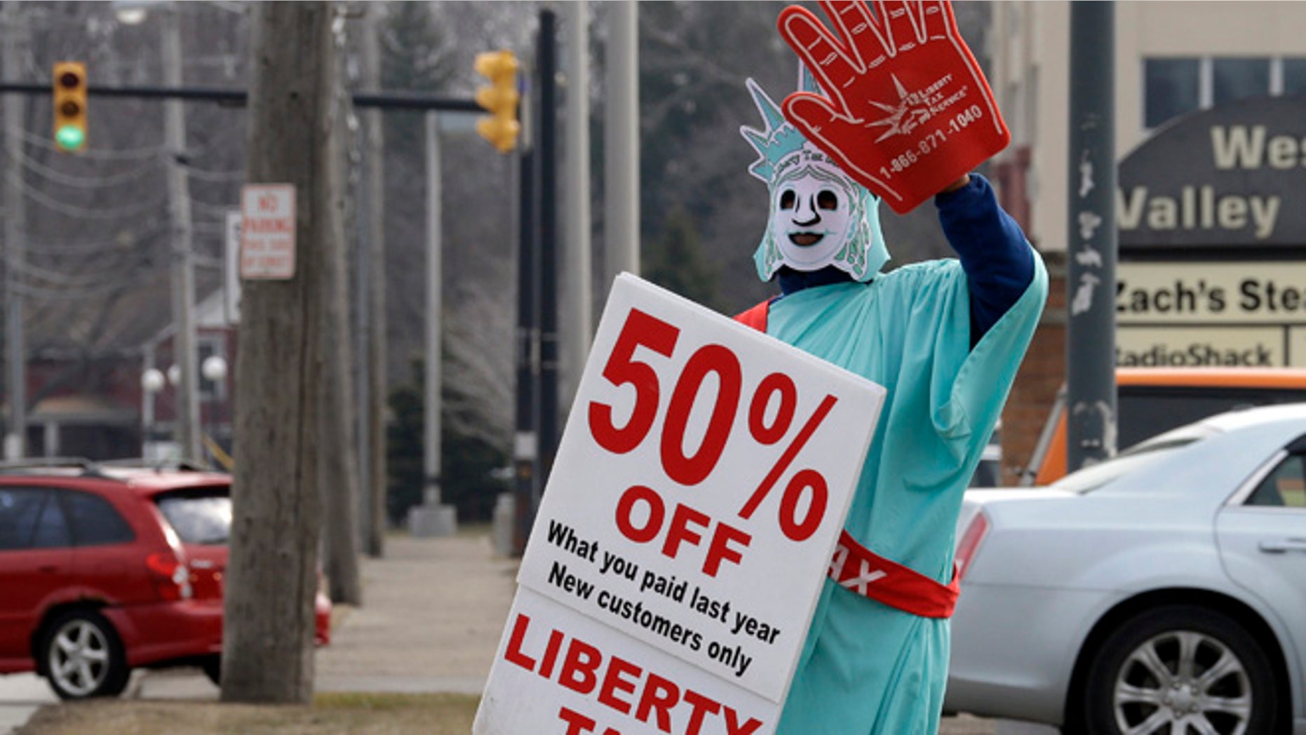 In this March 21, 2015 photo, Brittney Freison, dressed as Lady Liberty, waves to motorists near the Liberty Tax Service office in Berea, Ohio. Wary of rising fees, federal regulators are eyeing ways they can assert tighter oversight upon paid tax preparers who cater to an expanding market of cash-strapped families anxious for their tax refunds. (AP Photo/Mark Duncan)