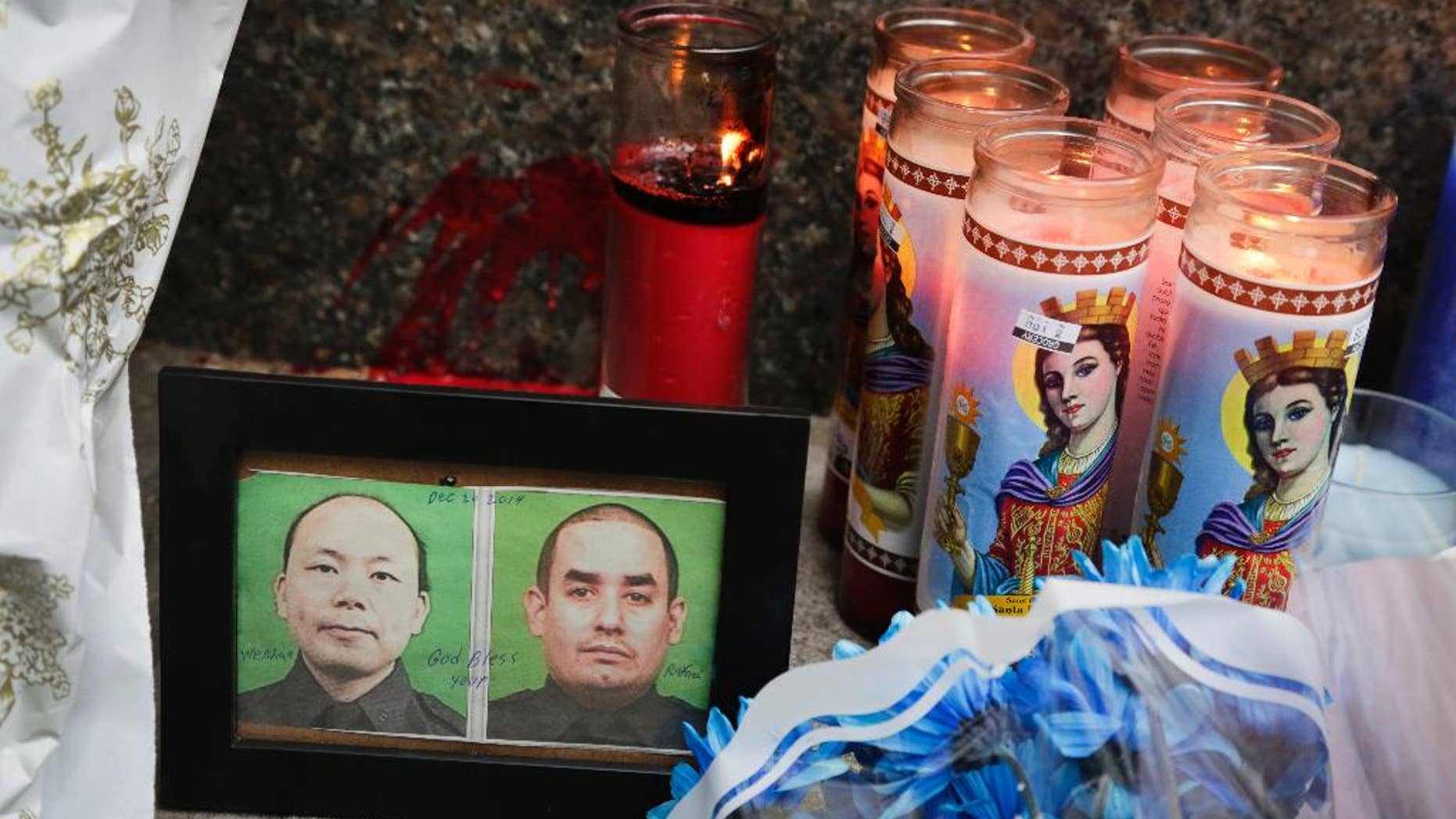Photographs of slain New York Police officers Wenjian Liu, left, and Rafael Ramos are placed in a makeshift memorial honoring the men at the 84th Precinct in the Brooklyn borough of New York, where the officers were stationed, Sunday, Dec. 21, 2014. Ismaaiyl Brinsley, who vowed online to shoot two "pigs" in retaliation for the police chokehold death of Eric Garner, ambushed Ramos and Liu in a patrol car Saturday and fatally shot them in broad daylight before running to a subway station and killing himself, authorities said. (AP Photo/Mark Lennihan)