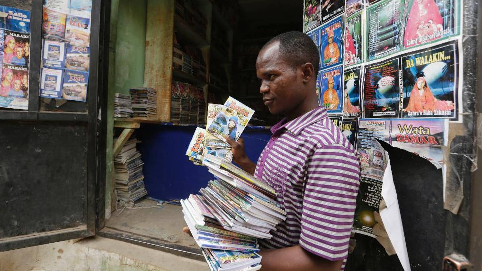 In this photo taken Monday April, 4. 2016, a Book hawker, Adamu Saidu, displays books he purchased at Kurmi Market to be sold in villages inaccessible by car in Kano, Nigeria. In the local market stalls are signs of a feminist revolution with piles of poorly printed books by women, as part of a flourishing literary movement centered in the ancient city of Kano, that advocate against conservative Muslim traditions such as child marriage and quick divorces. dozens of young women are rebelling through romance novels, many hand-written in the Hausa language, and the romances now run into thousands of titles. (AP Photo/Sunday Alamba)