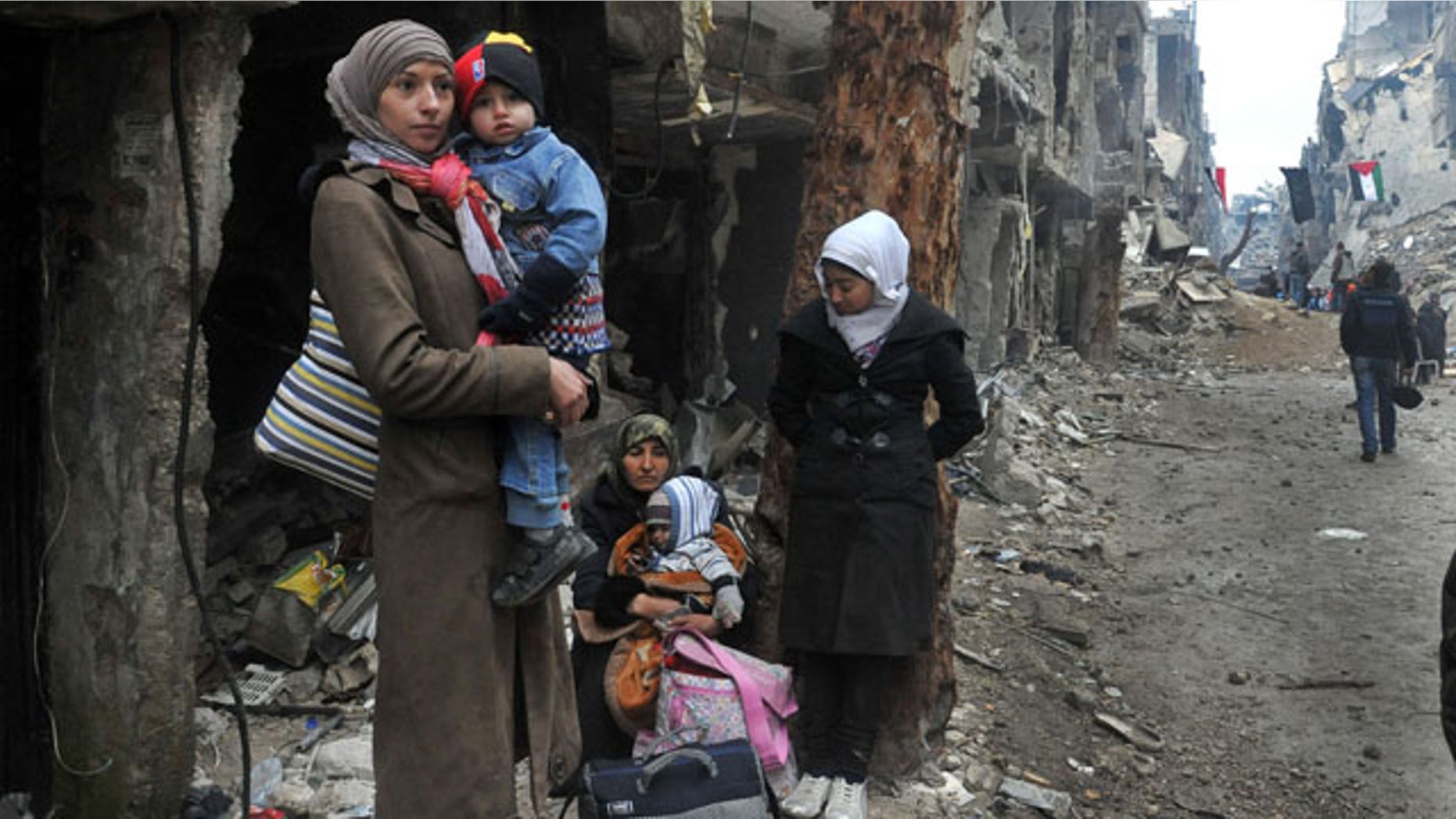 February 4, 2014: In this photo released by the Syrian official news agency SANA, residents of the besieged Yarmouk Palestinian refugee camp wait to leave the camp, on the southern edge of Damascus. Over the past six days the U.N. continued to distribute food parcels in the Palestinian camp where activists say at least 85 people have died as a result of lack of food and medicine since mid-2013. (AP Photo/SANA)