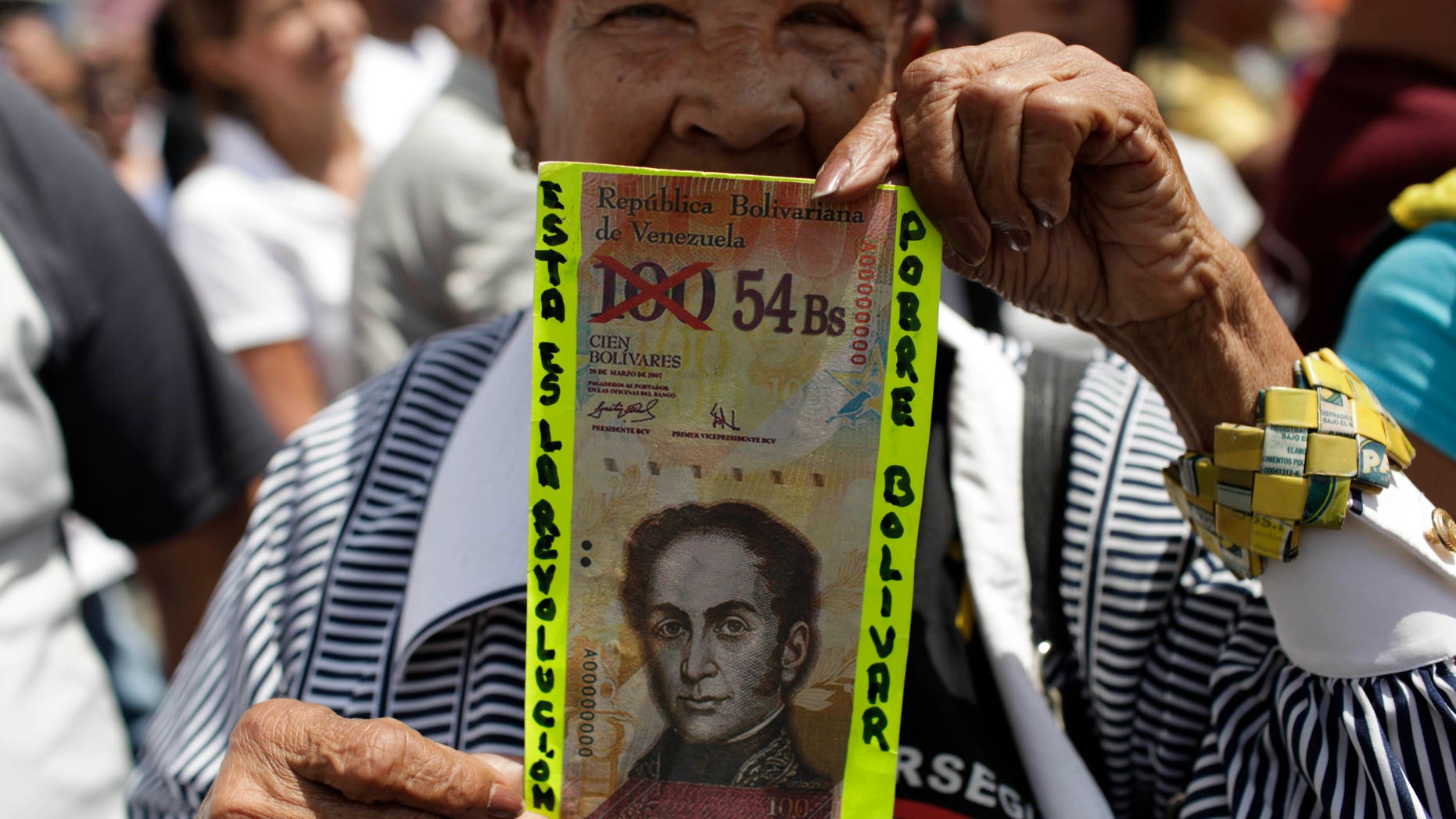 FILE - In this Feb. 23, 2013 file photo, an anti-government protester in Caracas holds up a fake Venezuelan banknote that reads in Spanish, "This is the revolution. Poor Bolivar," with the value of 100 crossed out and 54 written next to it. Venezuelans have been scrambling for dollars as their bolivar currency is in free fall, selling on the black market for a tenth its official value. In response, the government is trying to block access to websites that Venezuelans use to track the black market exchange rate. (AP Photo/Ariana Cubillos, File)