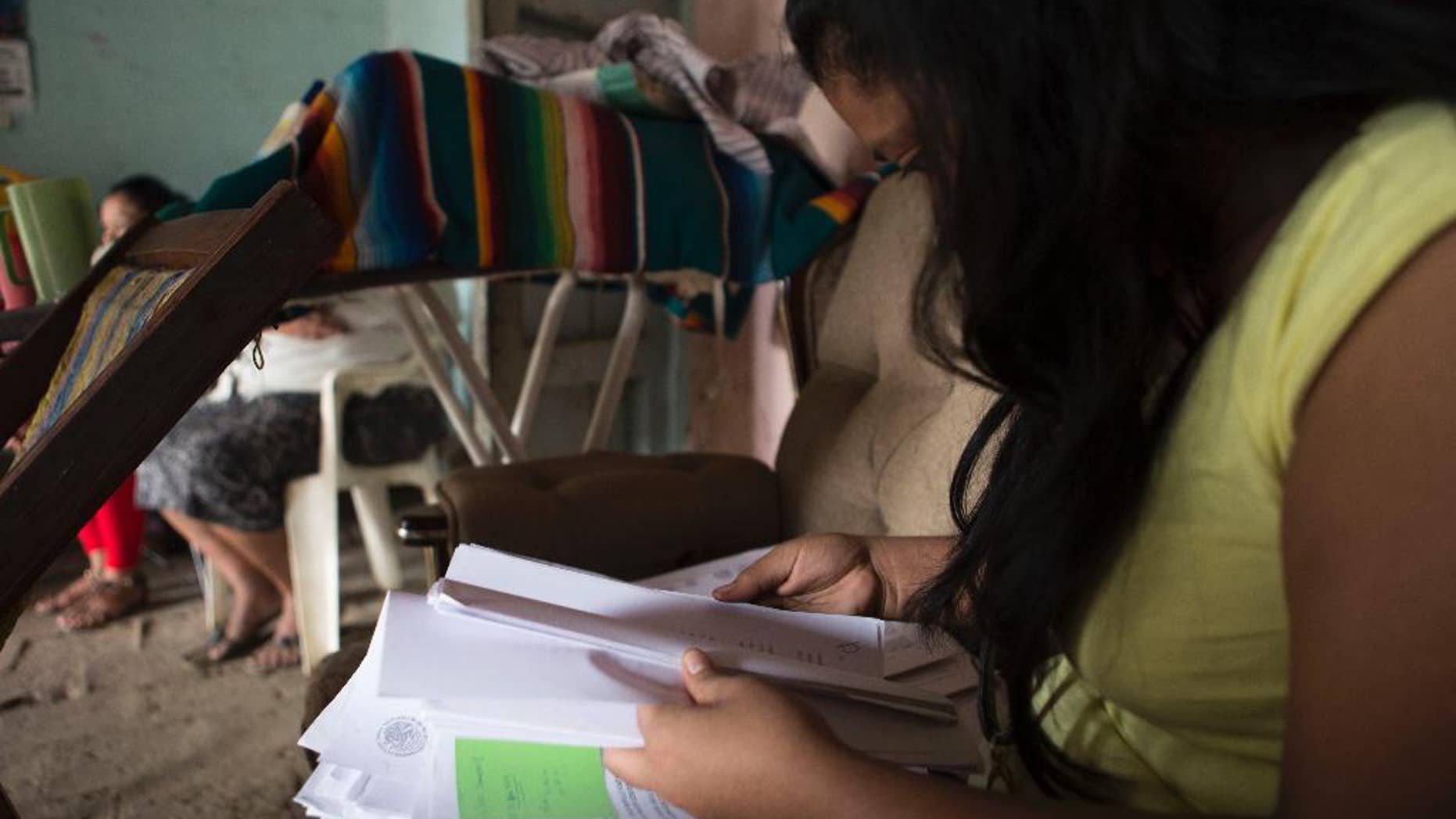FILE - In this Dec. 23, 2014 file photo, a woman who spoke on the condition of anonymity in fear retribution by officials and drug traffickers, looks through court documents at her home in Arcelia, Mexico, during her first interview since being tortured and falsely imprisoned for five months on weapons possession charges. The Mexican government said Thursday, May 14, 2015 it will give at least 50 million pesos ($3.3. million) to the relatives of criminal suspects slain in 2014 by soldiers and survivors of the shootings, after a rights investigation found 12 to 15 of the 22 suspects were killed by army troops after surrendering. The investigation found the victims included three women who survived the attack and were tortured or pressured to support the army's version that all 22 suspects were killed in a shootout. (AP Photo/Christian Palma, File)